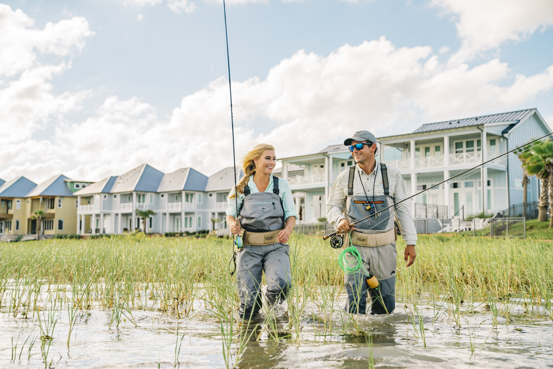 Man woman walking through marsh in front of homes to fly fish