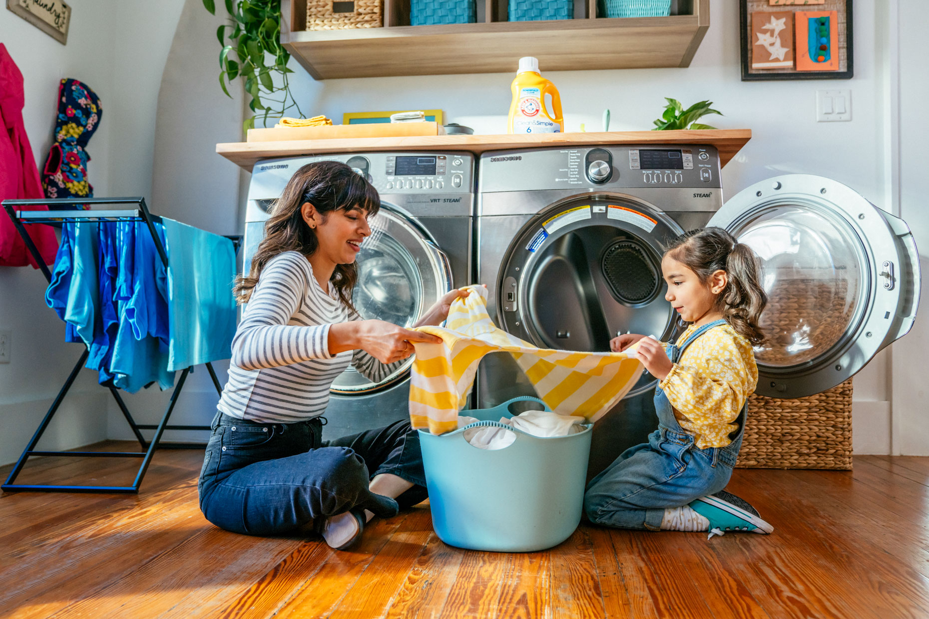 Mom and daughter folding laundry together on floor by washer dryer