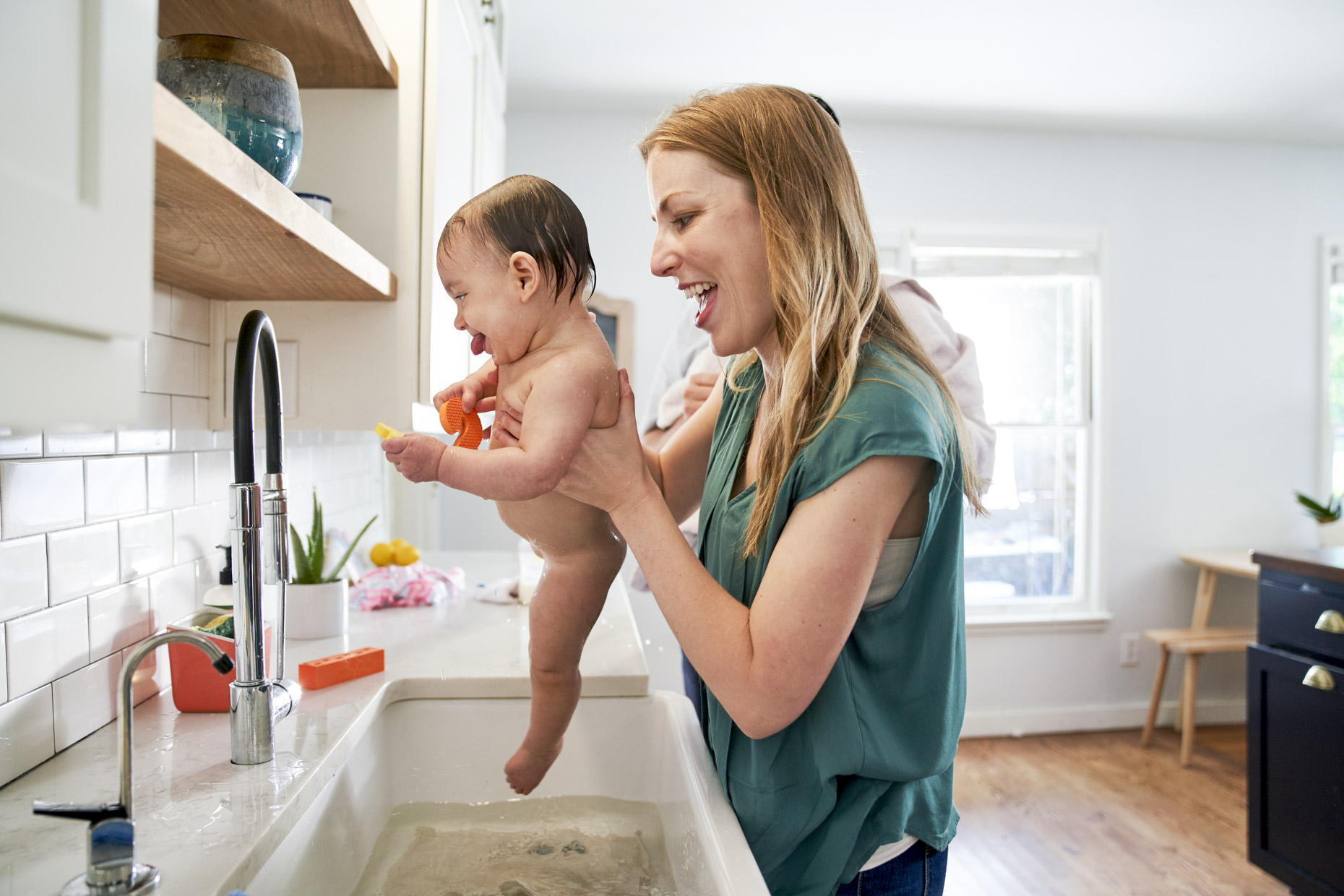 Happy mom lifting baby out of kitchen sink bath