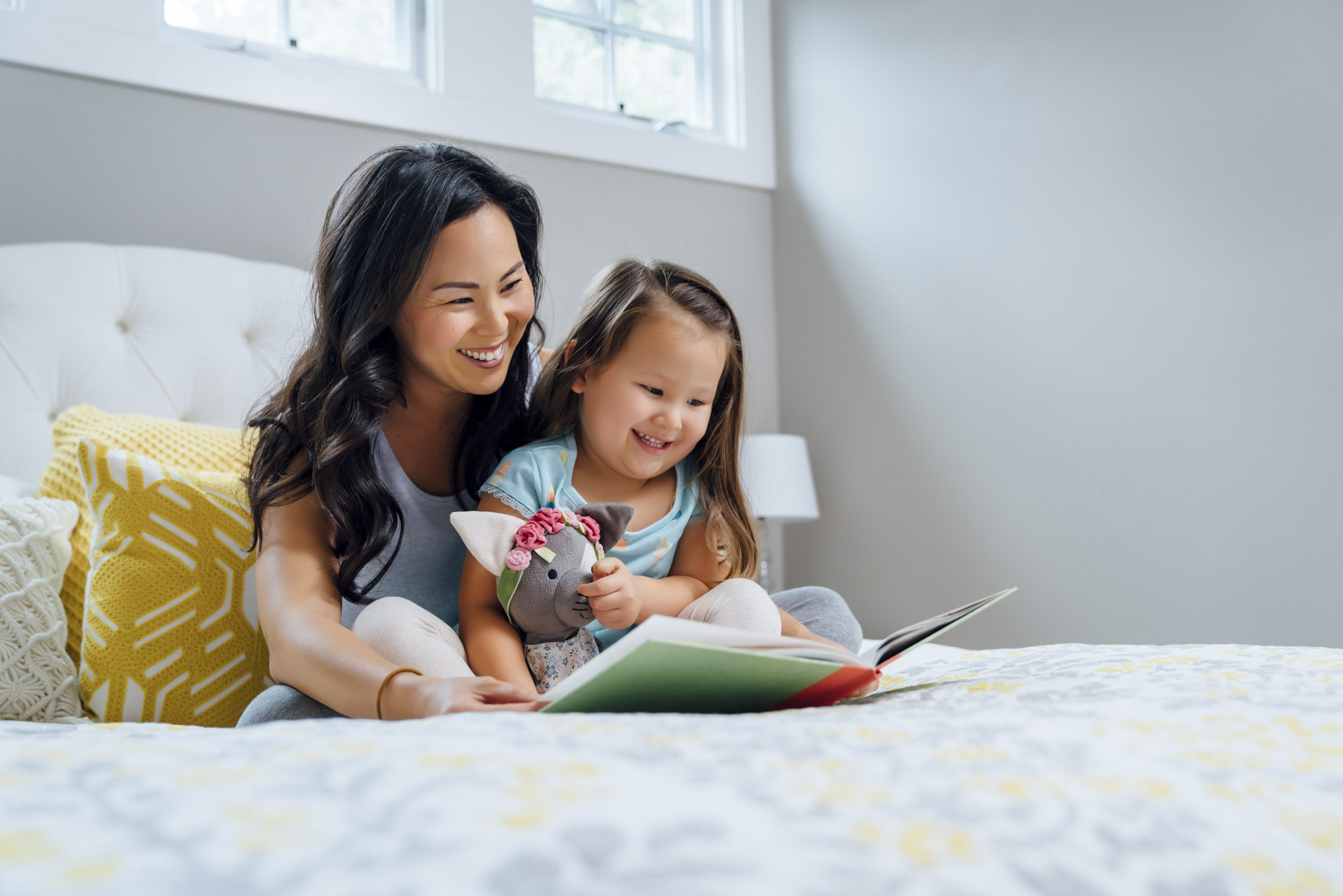 Mom reading book to daughter sitting on bed
