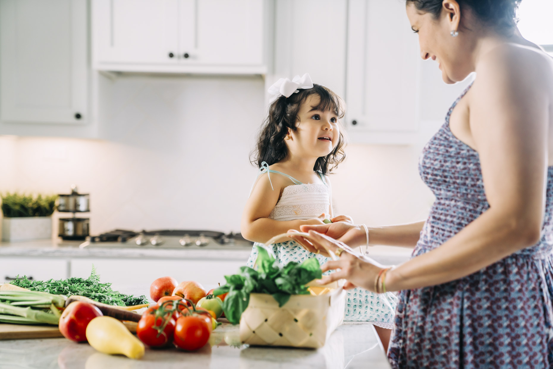 Mom unloading basket of vegetables with daughter on counter