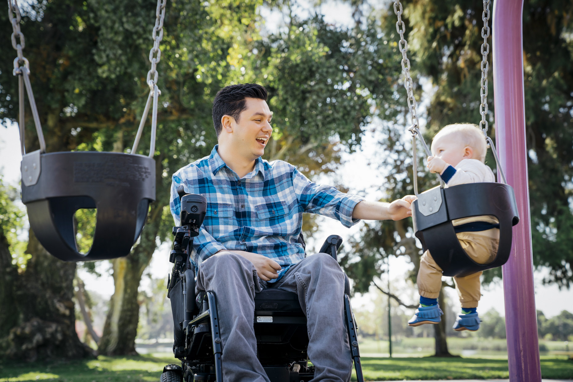 Parapalegic man in wheel chair pushing baby in swing in park