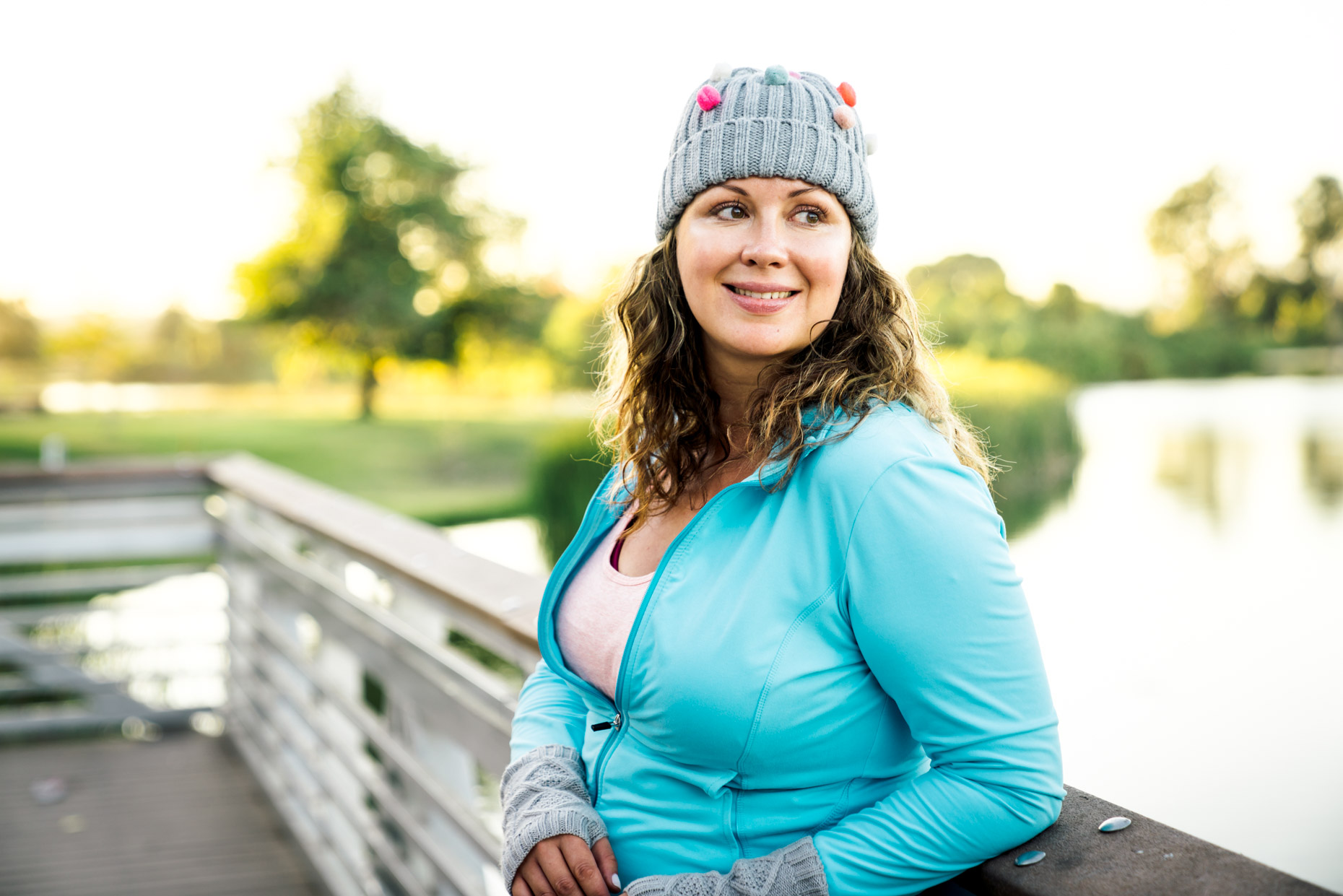 Plus-sized woman in fitness attire and hat standing on bridge smiling 