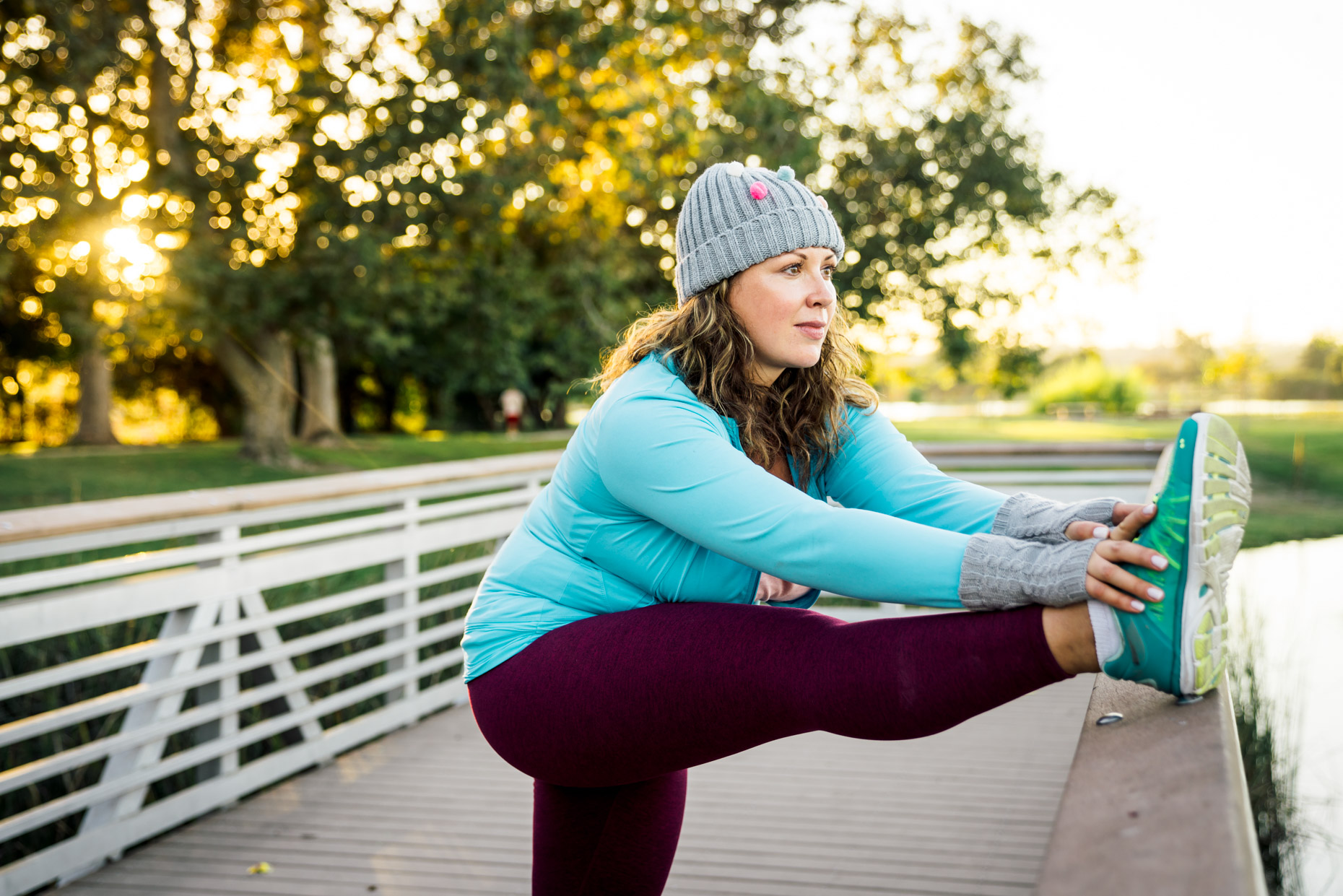 Plus-sized woman in fitness attire and hat stretching on bridge in park in fall