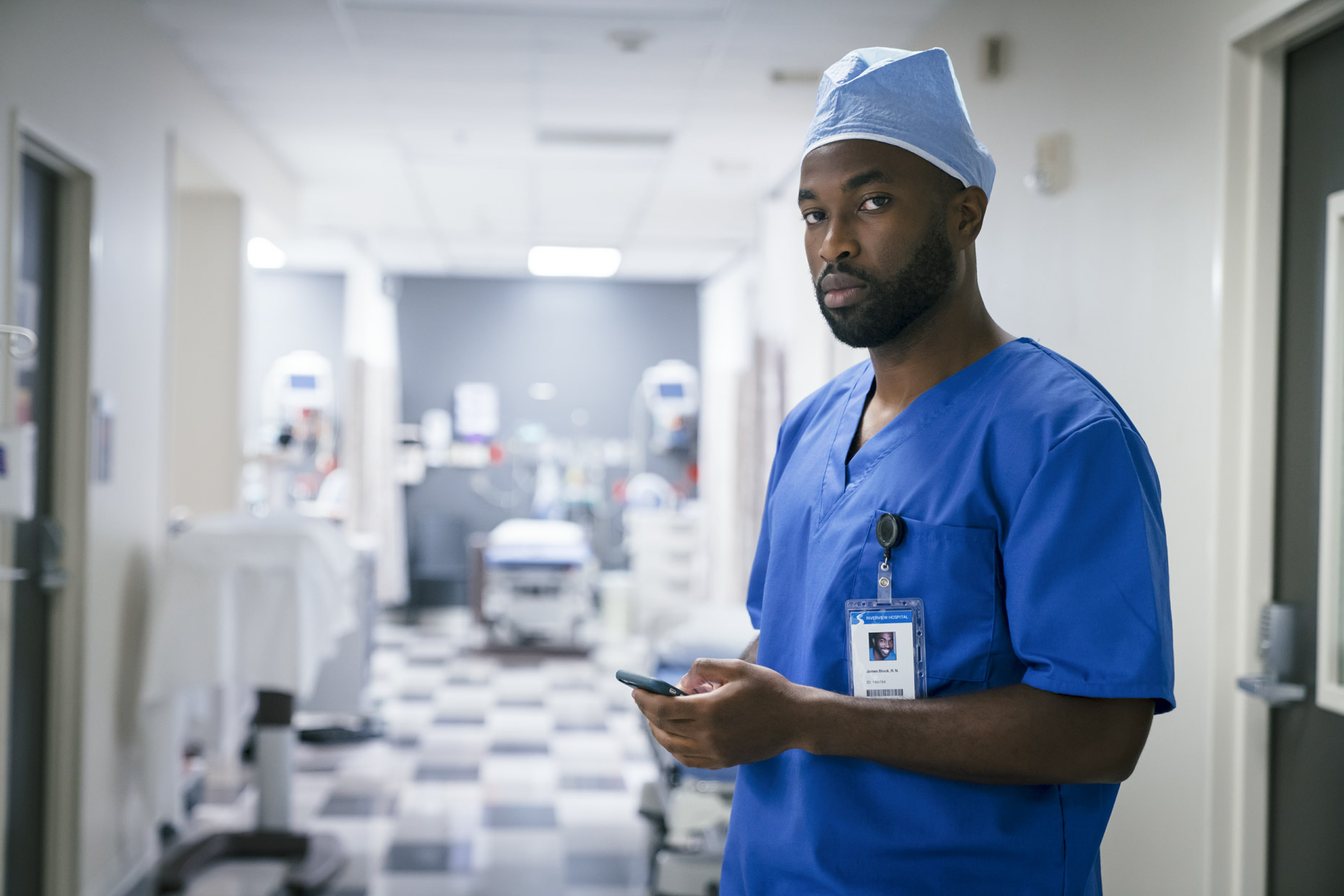 Portrait of black male surgeon in scrubs in hospital holding cell phone