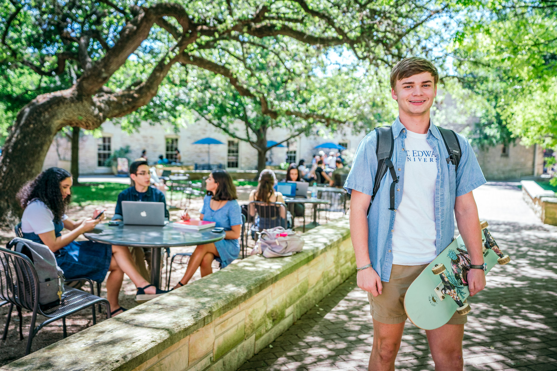 Portrait of male college student holding skateboard outside on college campus