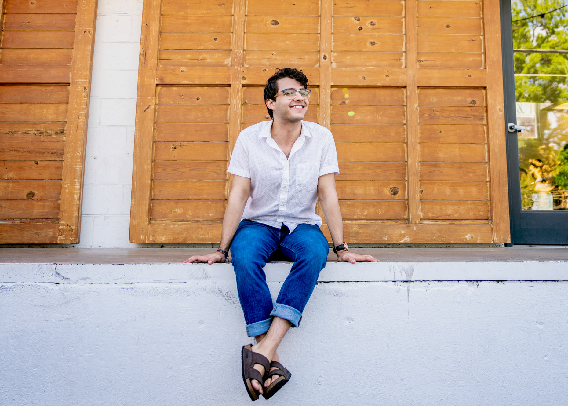 Portrait of smiling young man in glasses sitting on wall