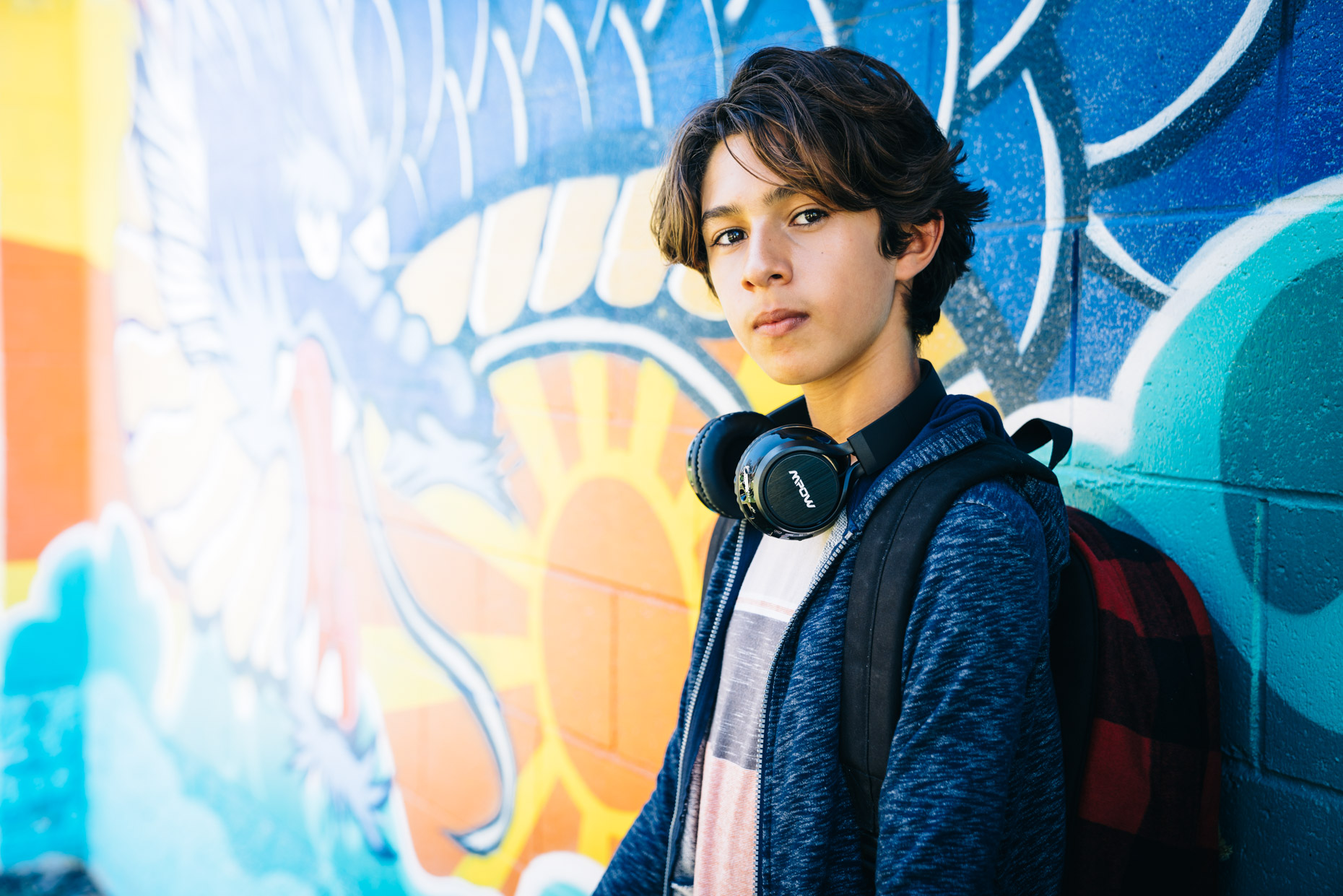 Portrait of teen boy leaning on grafitti wall with headphones around neck