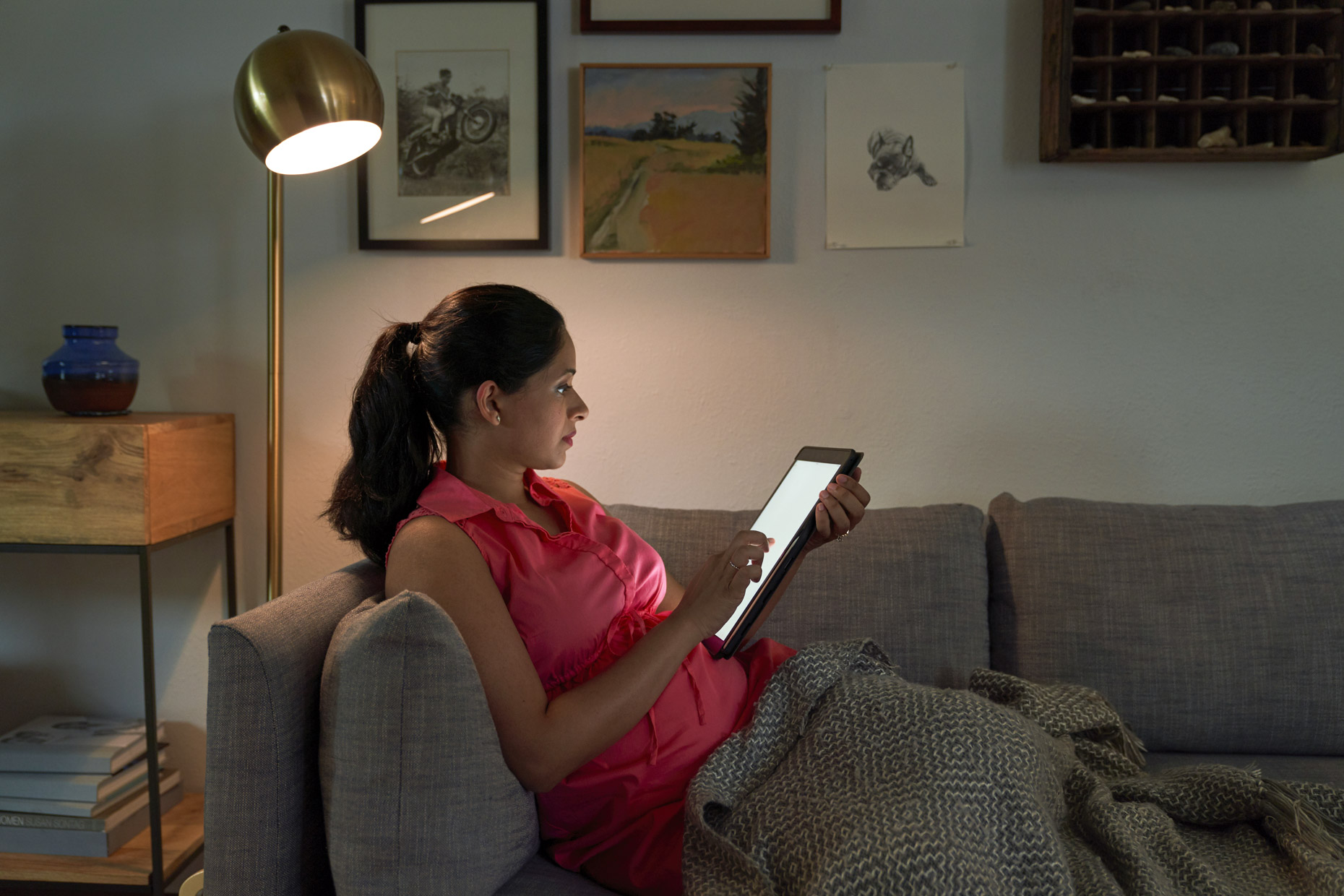 Pregnant woman sitting on the couch at night looking at ipad tablet computer