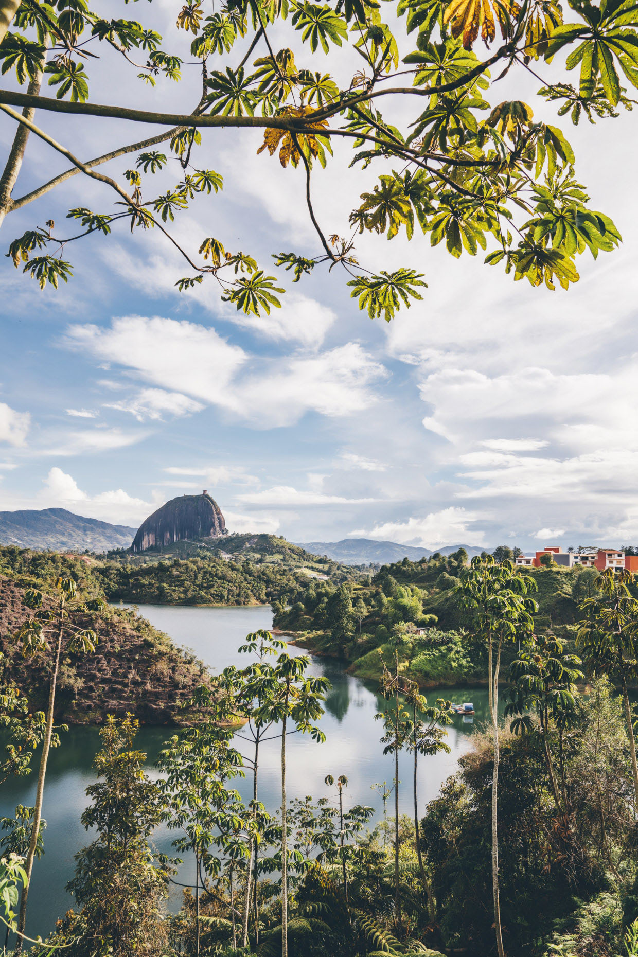 Rock of Guatape through tree leaves and across lake in Colombia