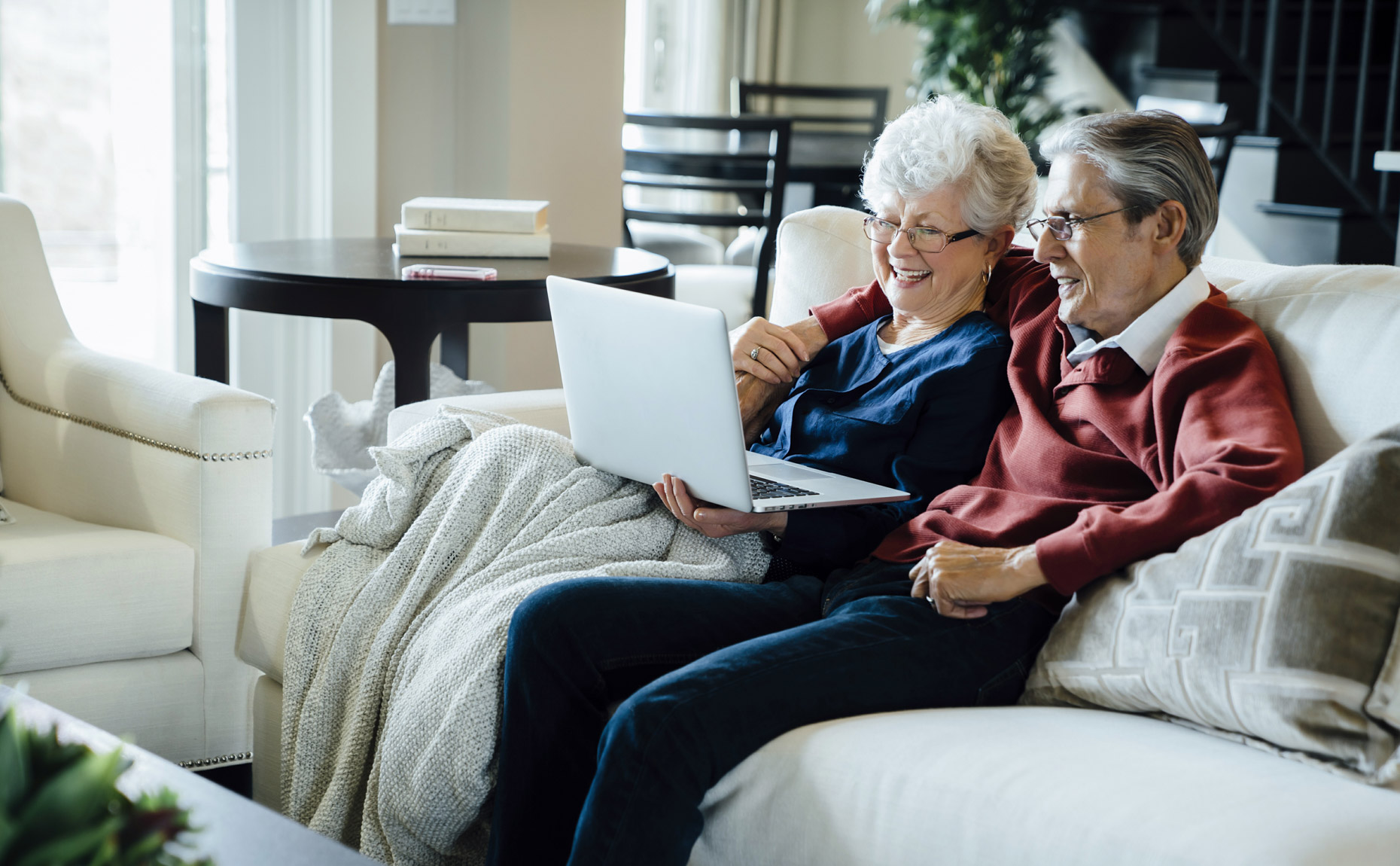 Senior couple snuggling on couch smiling at laptop