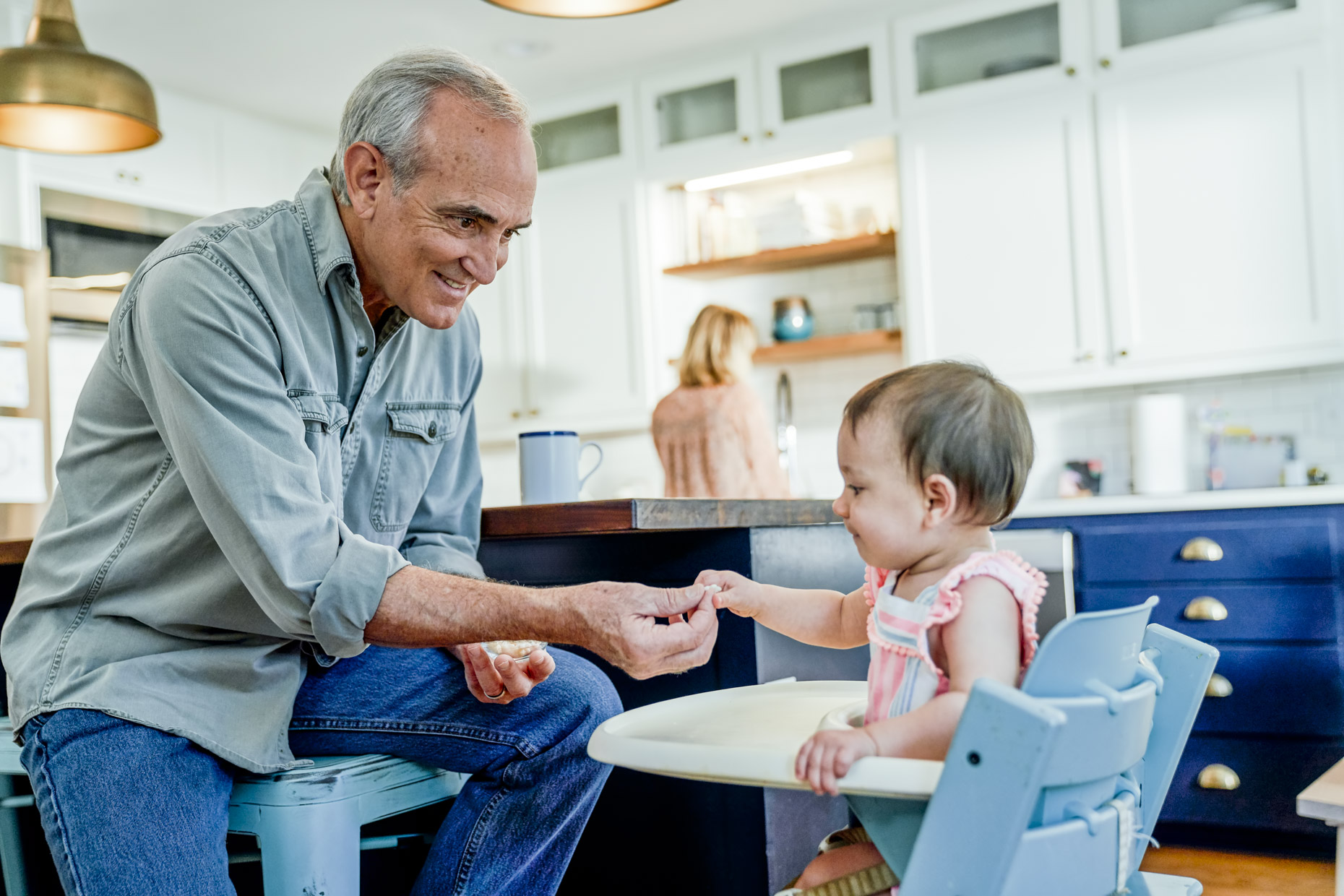 Senior man feeding granddaughter in high chair in kitchen
