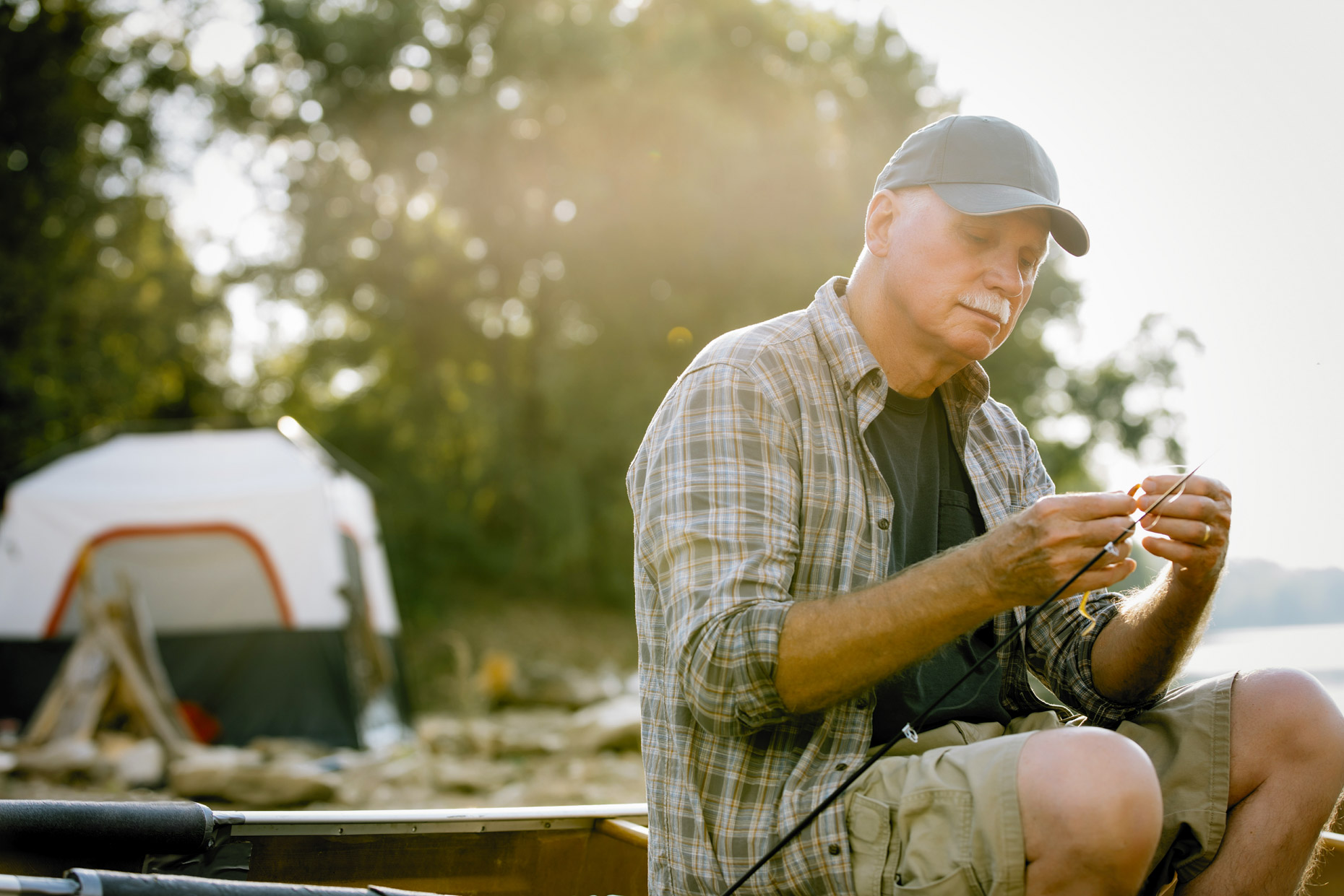 Senior man fishing by camping tent