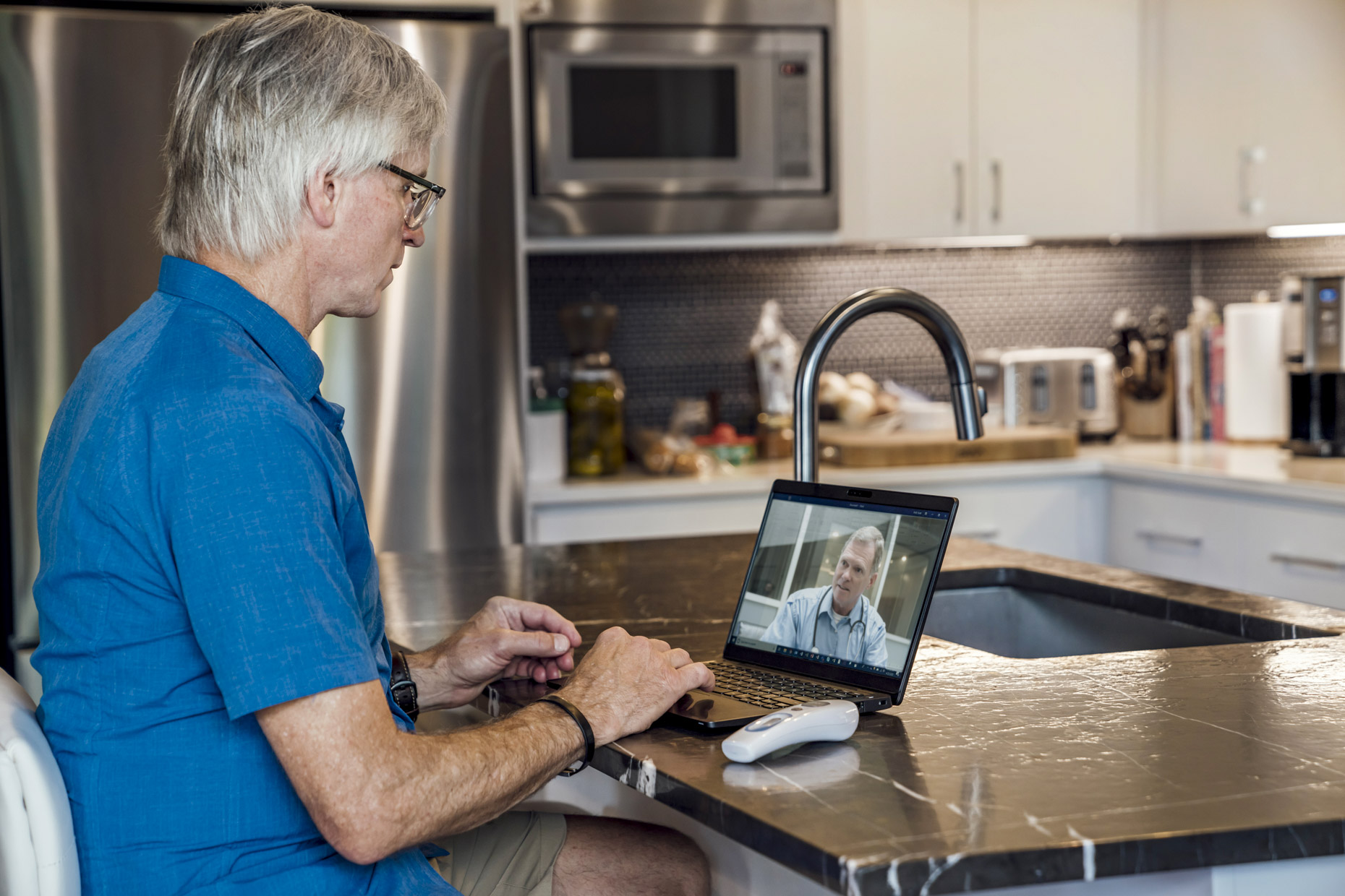 Senior man video chatting with doctor on laptop computer in kitchen