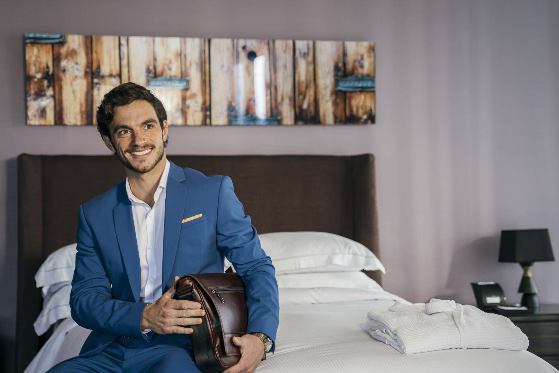 Smiling business man sitting on bed in Hilton Hotel room