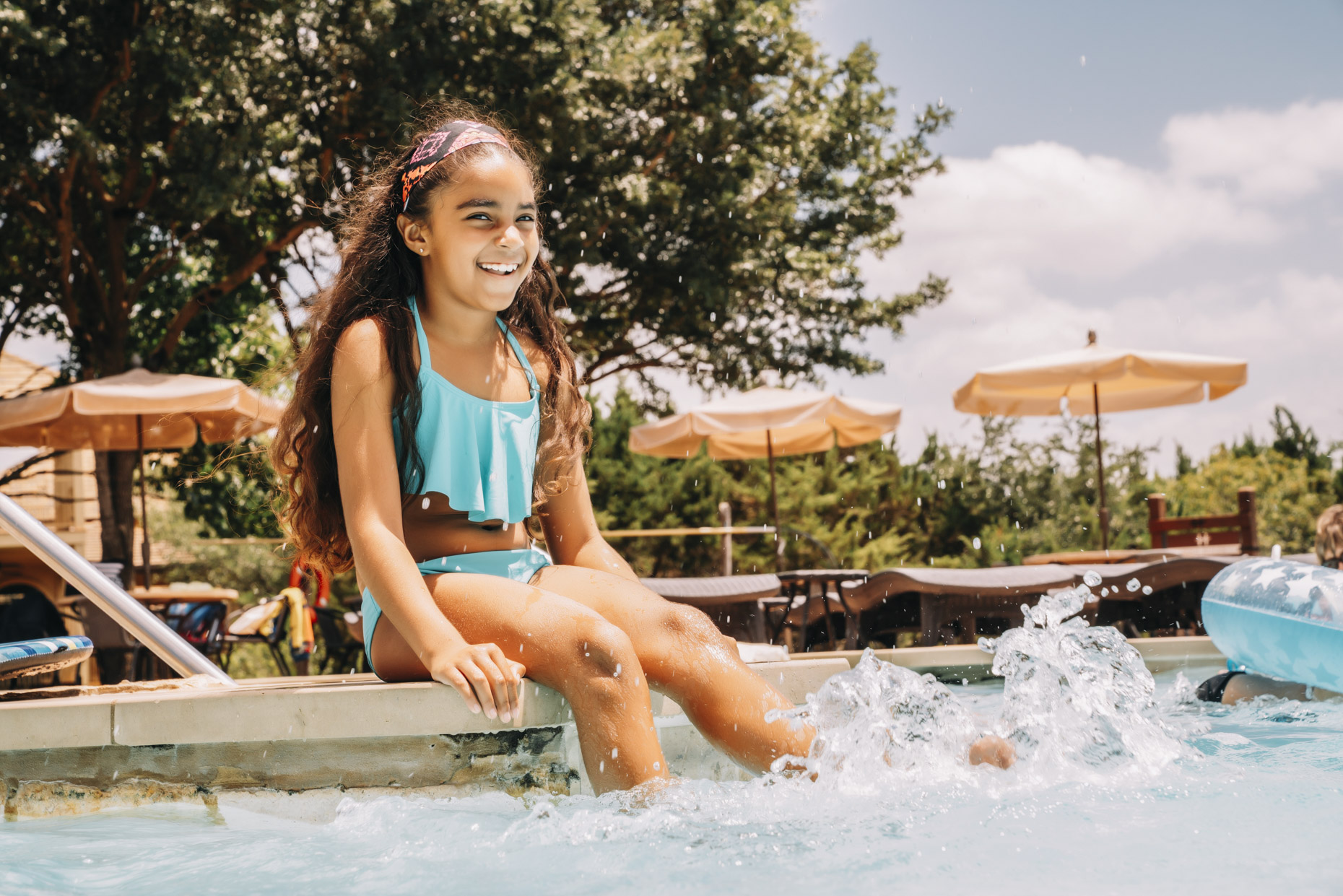 Smiling hispanic girl sitting poolside kicking water in pool