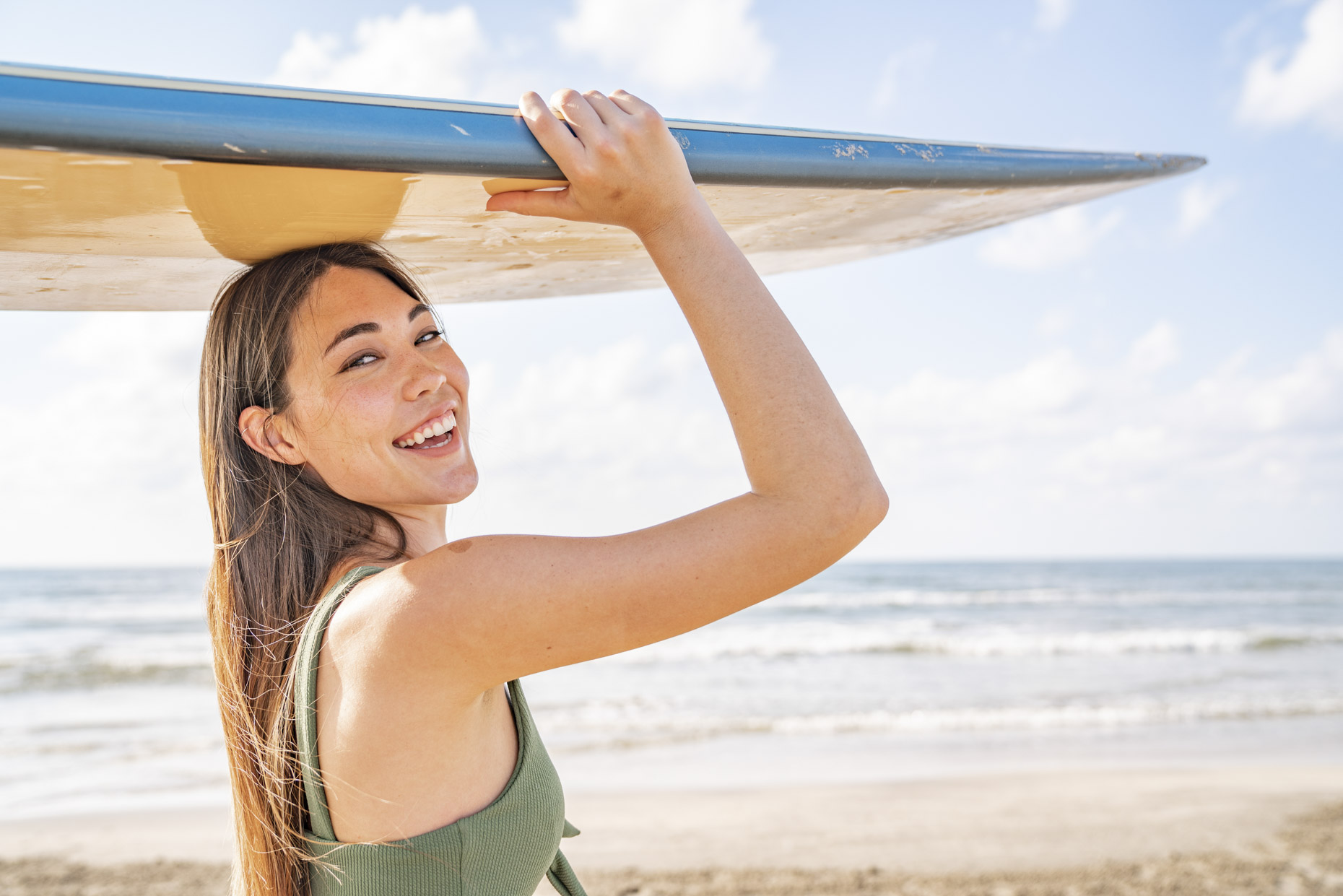 Smiling woman holding surfboard on head