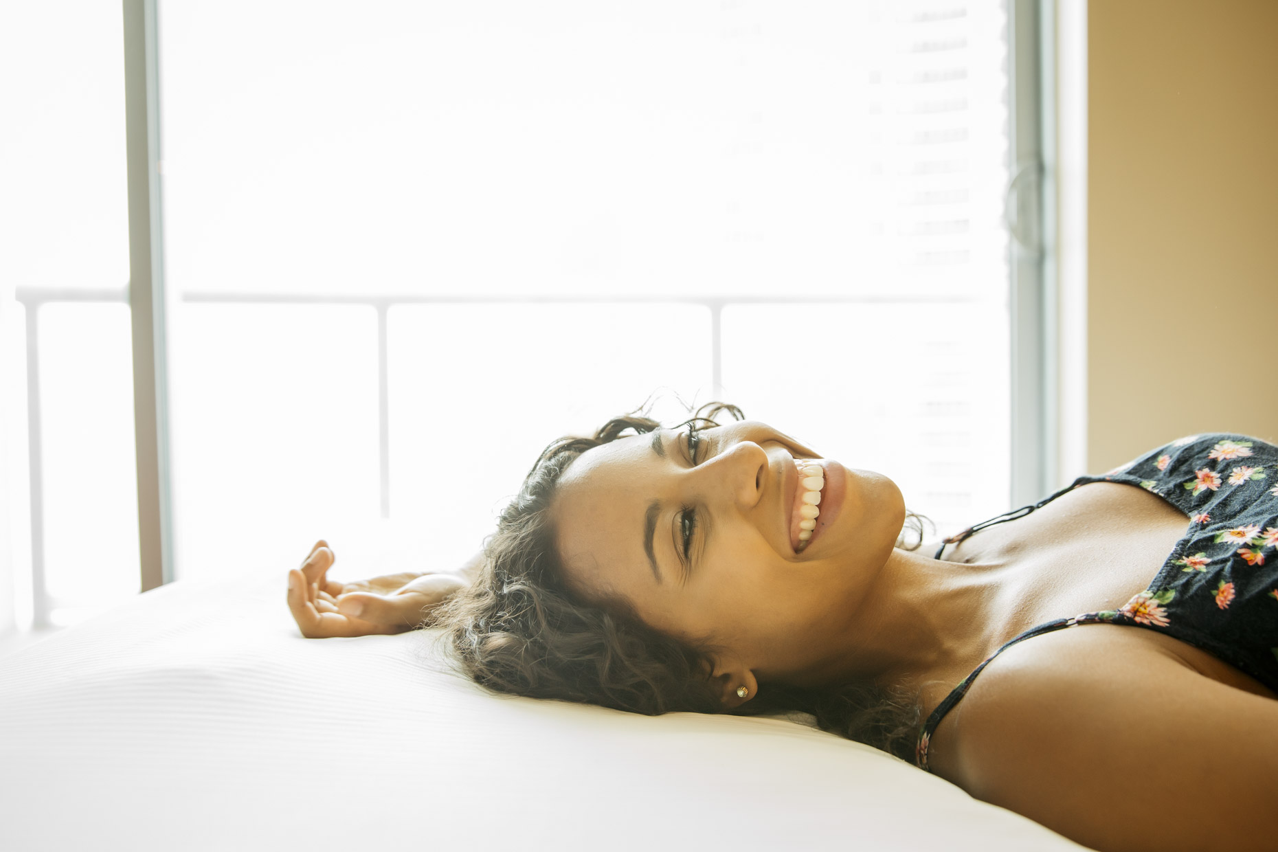 Smiling woman laying on her back on bed in hotel room 