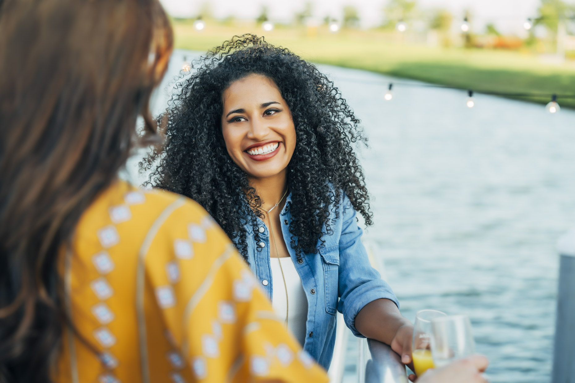 Smiling woman with big curly hair talking to friend by lake