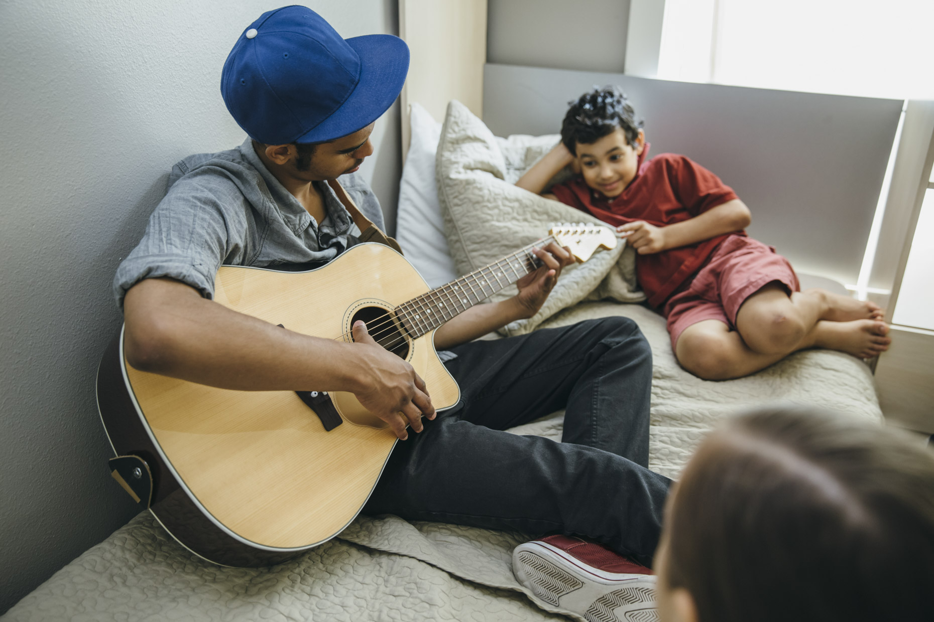 Teen boy on bed playing guitar for brother and sister