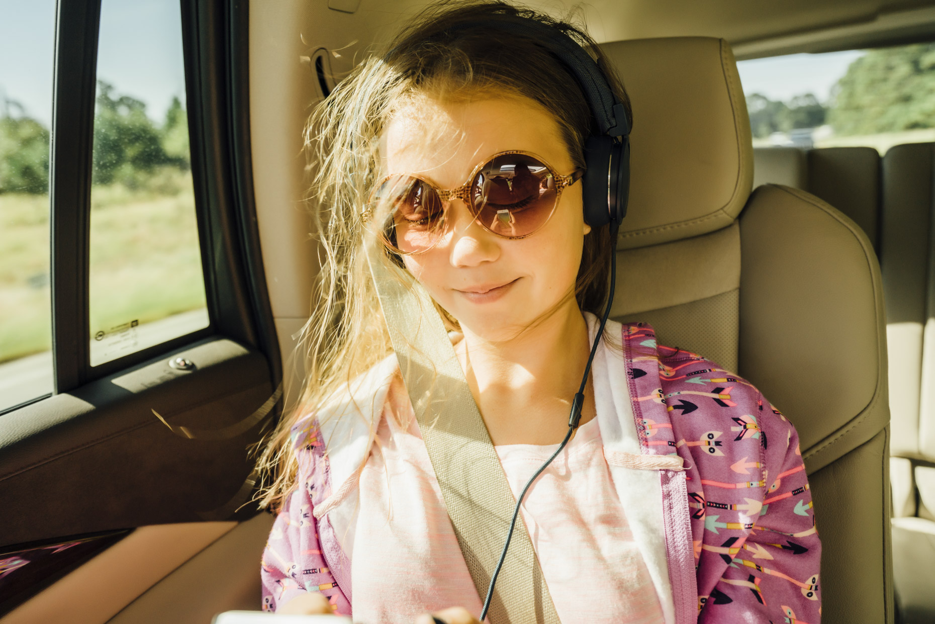 Teen girl in round glasses and headphones riding in car with hair blowing in the wind