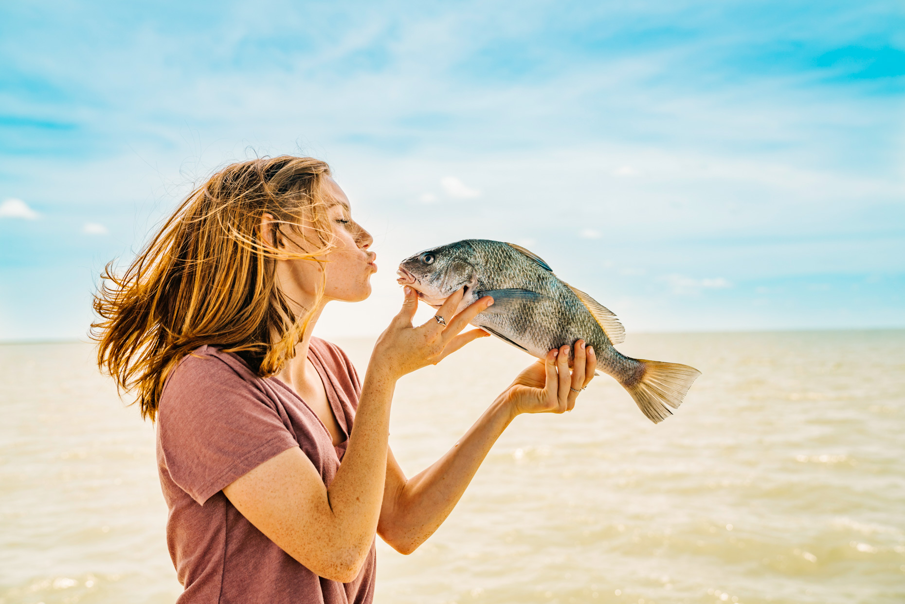 Red haired teen girl pretending to kiss fish