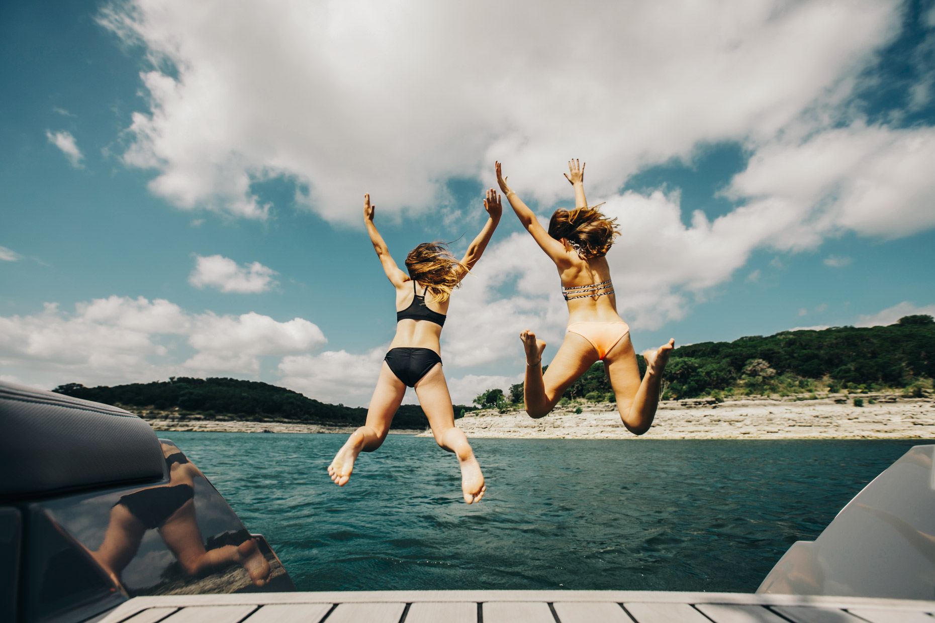 Teen girls jumping off of boat into lake