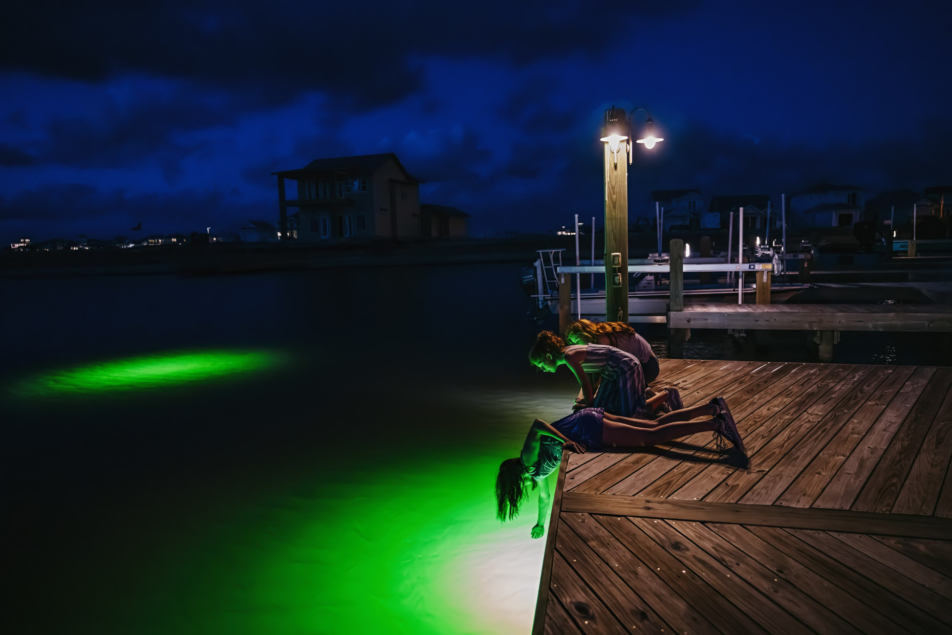 teen girls peering off of dock at night into green light in water
