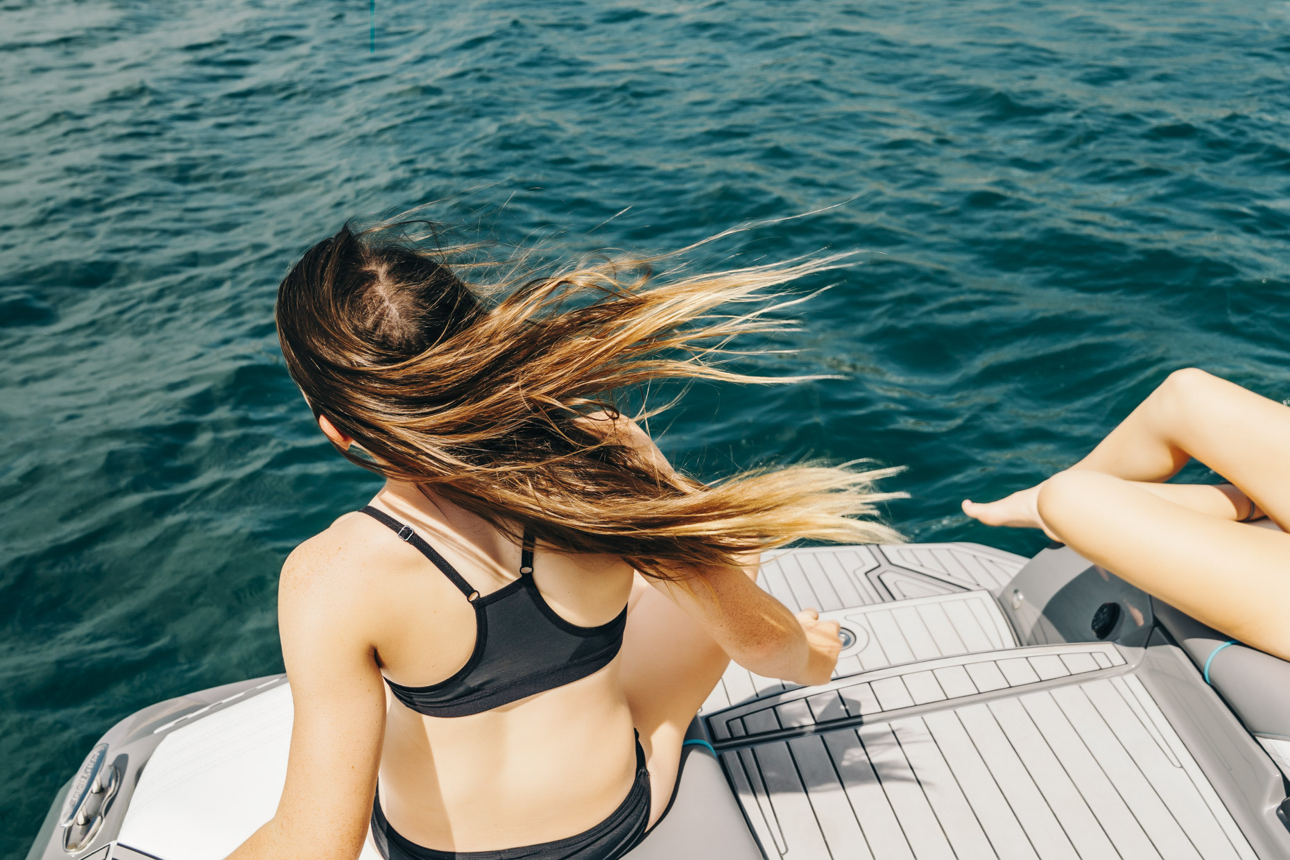 Teen sitting on edge of boat on lake with her hair blowing in the wind