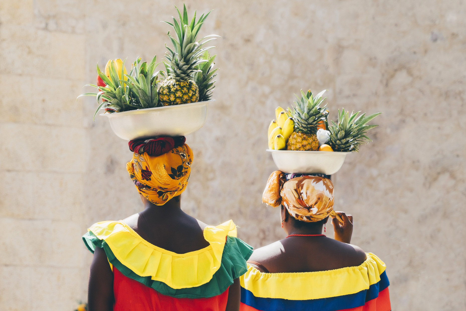 Women in colorful clothes carrying bowls of fruit on their heads