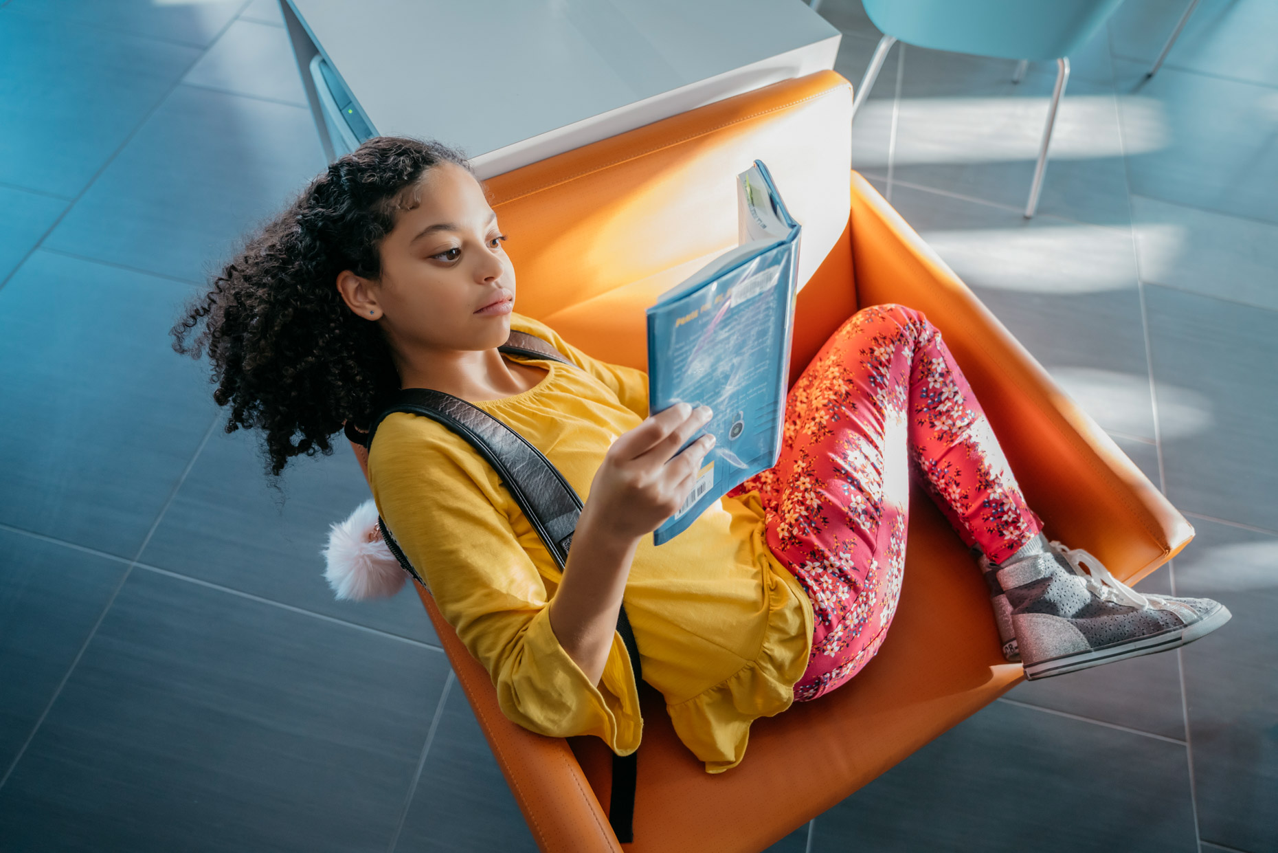 Tween girl reading book curled up in orange chair
