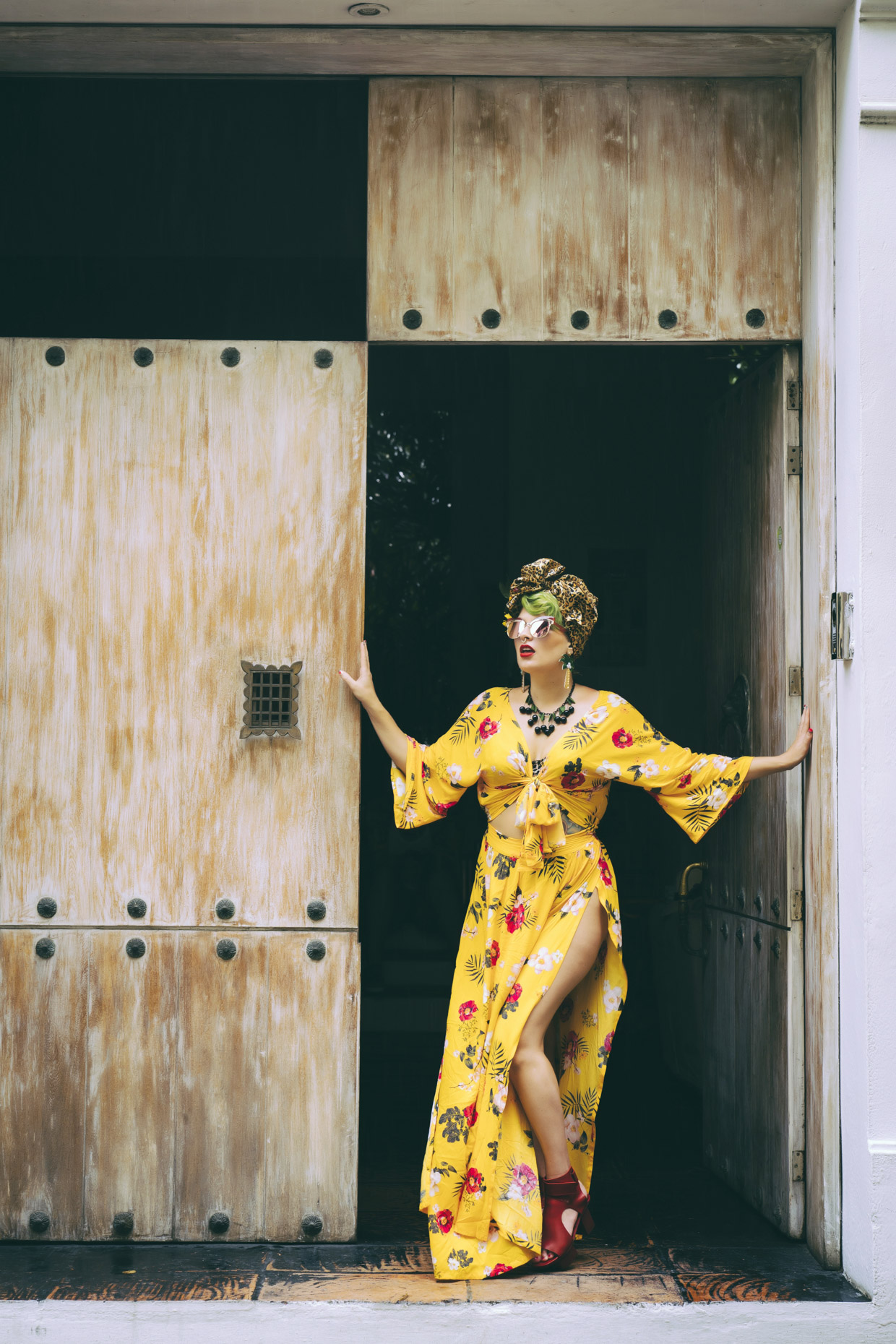 Woman in long floral dress and leopard print headwrap standing in doorway
