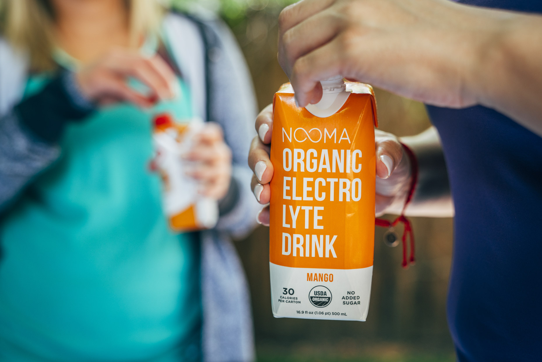 Woman in workout clothes holding Nooma mango electrolyte drink