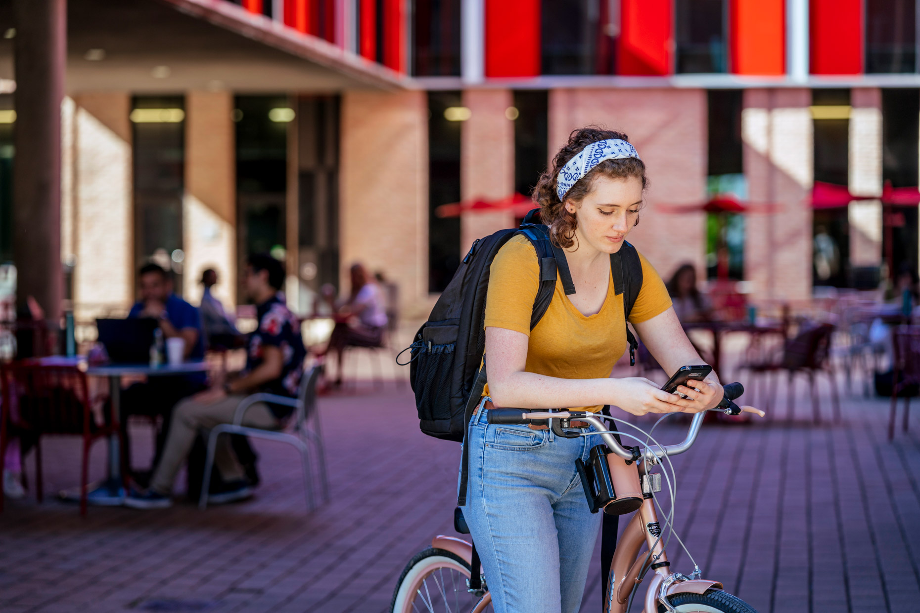 Woman on college campus resting with arms on bike handles texting on phone