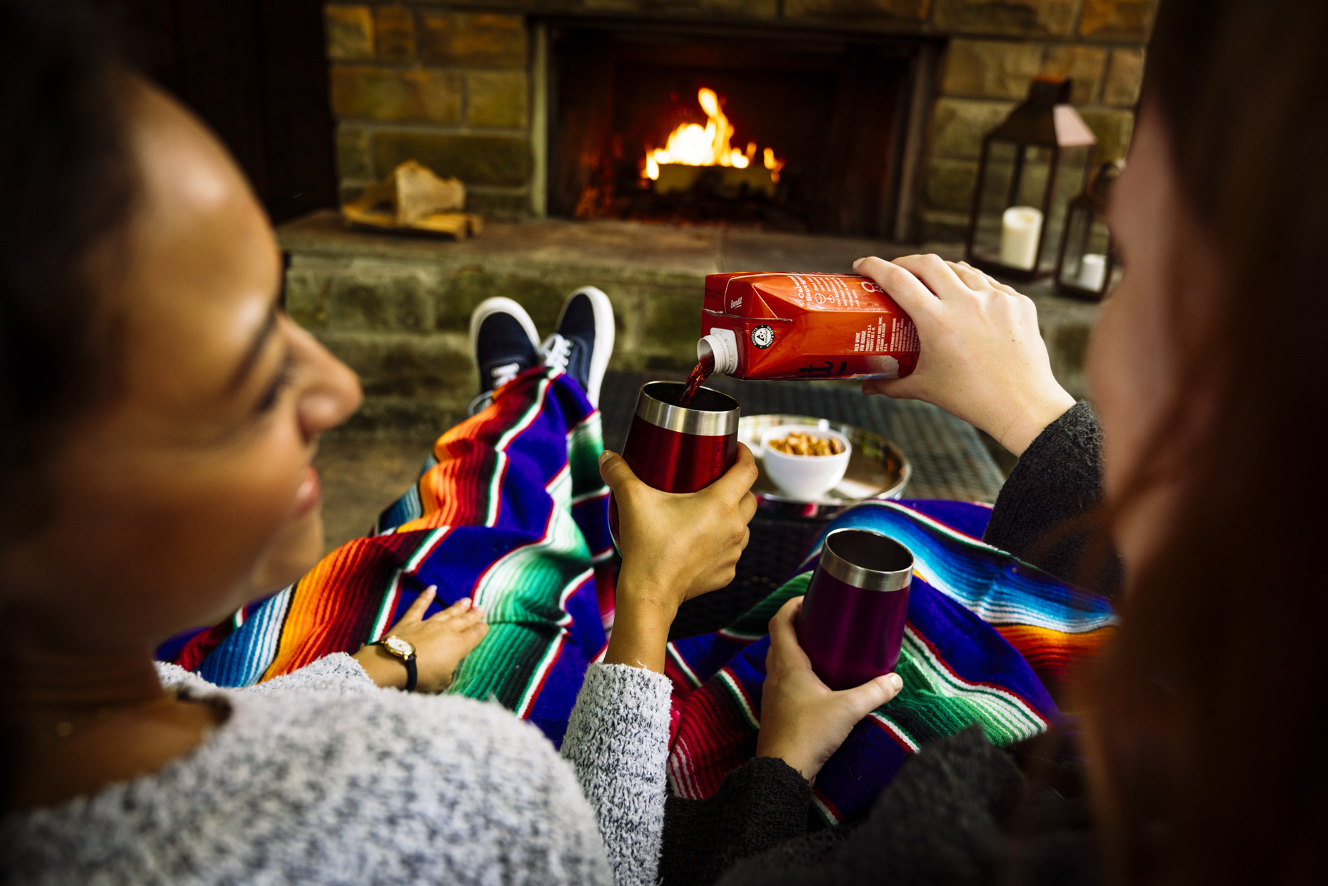 Woman pouring wine for girlfriend in front of fireplace