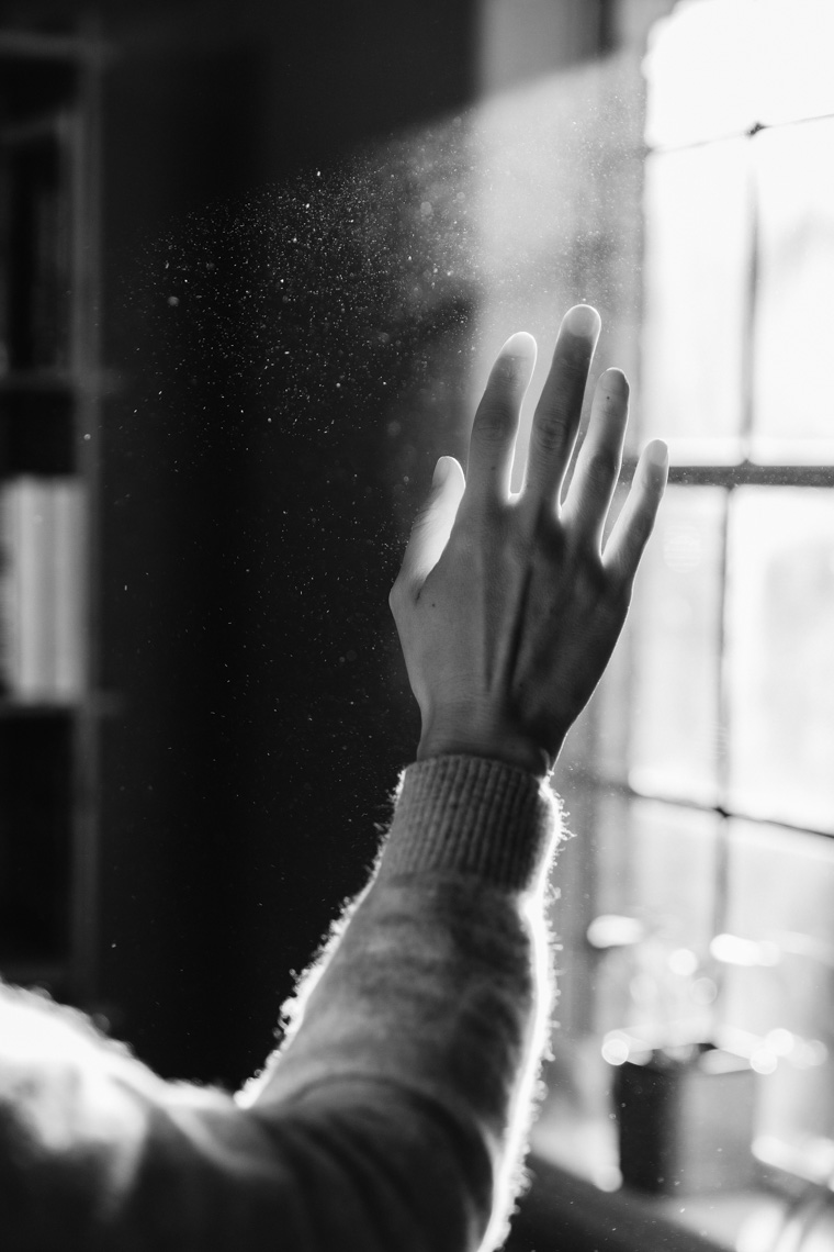 Woman putting hand up to light streaming through window