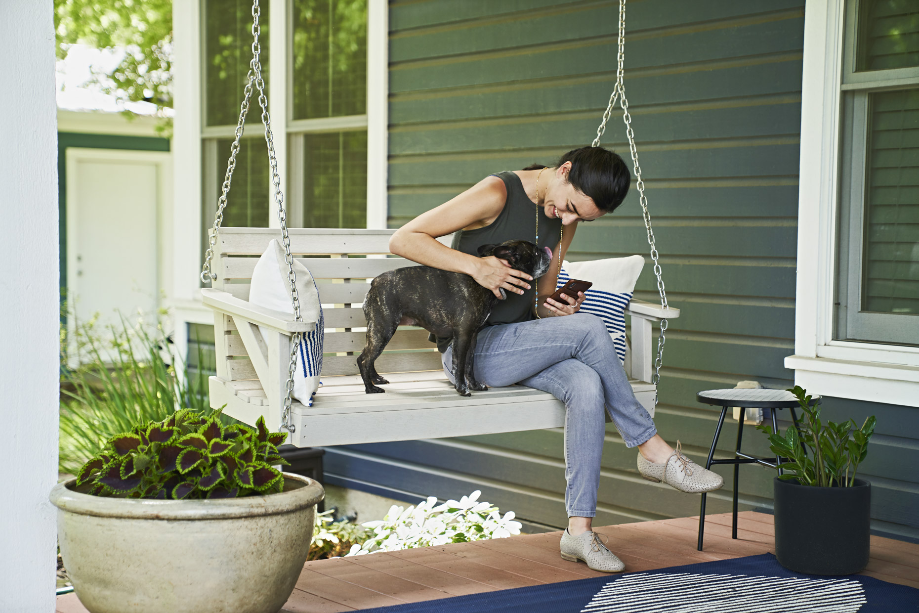 Woman sitting on porch swing petting her french bulldog