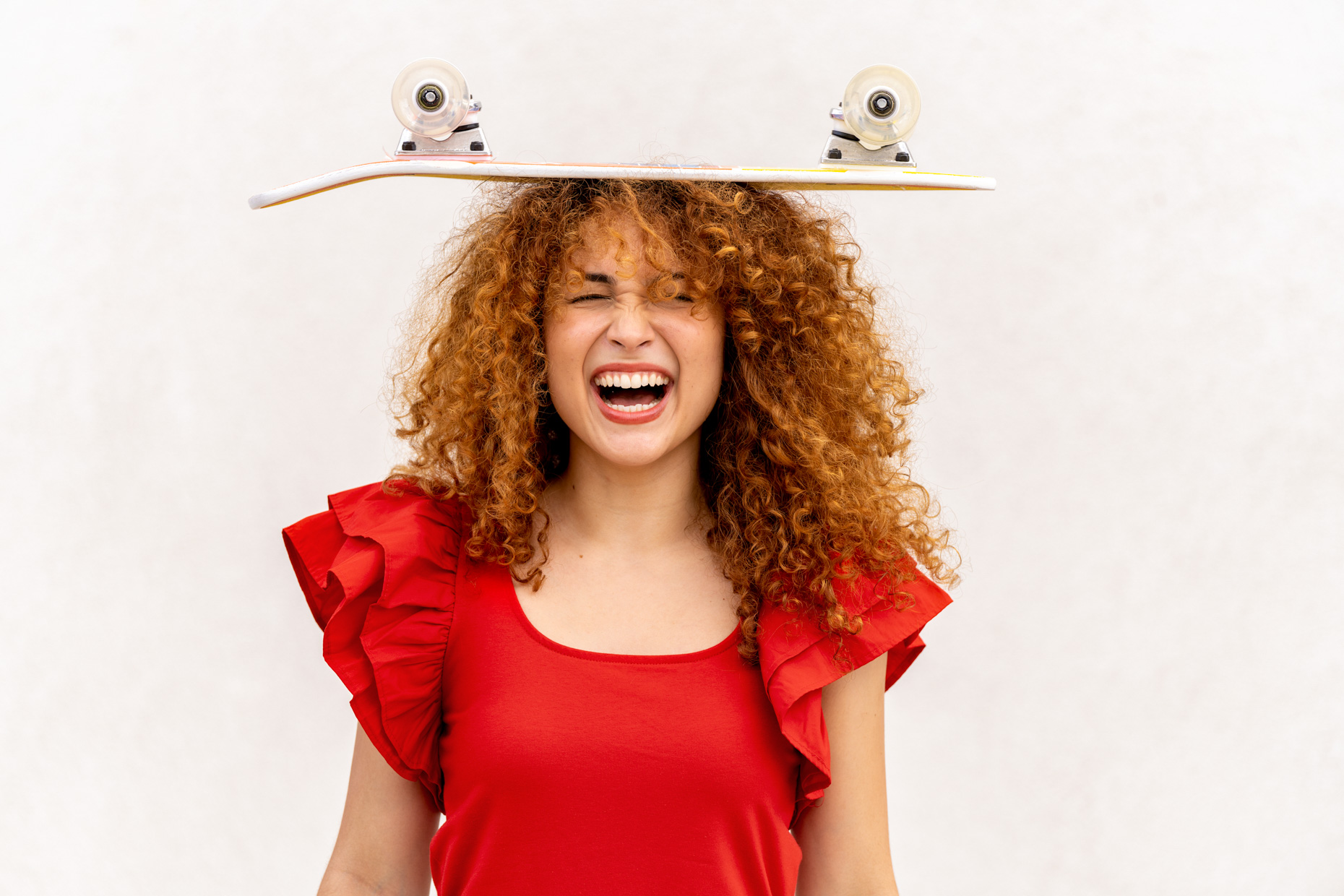 Woman-smiling-with-skateboard-on-her-head-red-shirt-042623_WILDLIGHT_SCENE5_8007-Edit