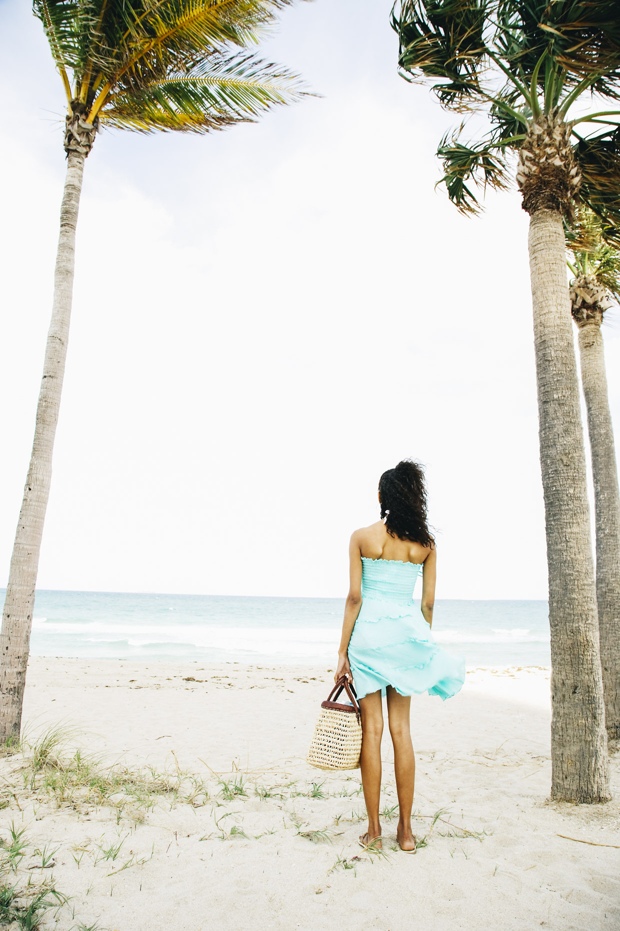 Woman standing on beach in blue dress looking at ocean