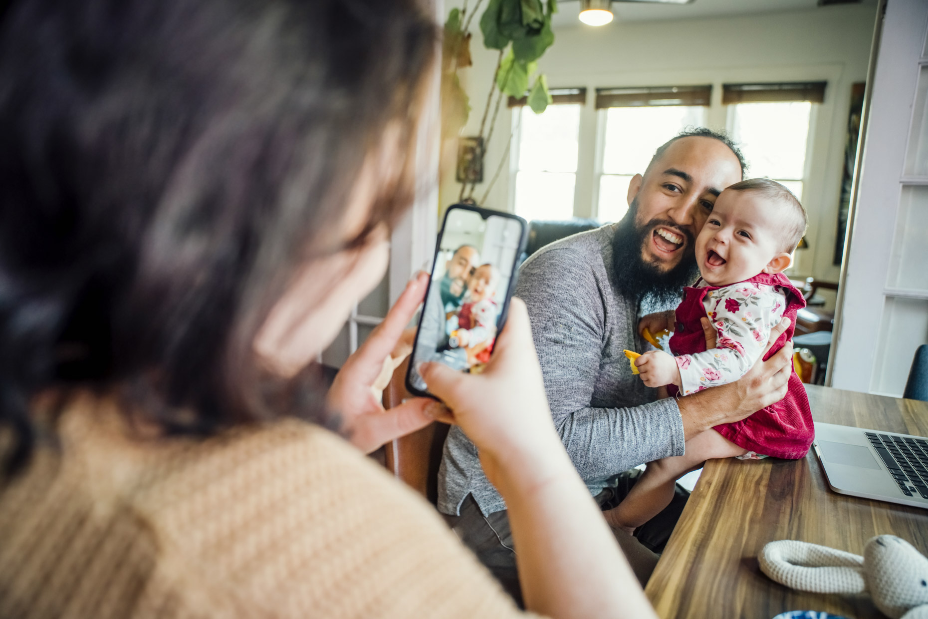 Woman taking photo of man and smiling baby with cell phone
