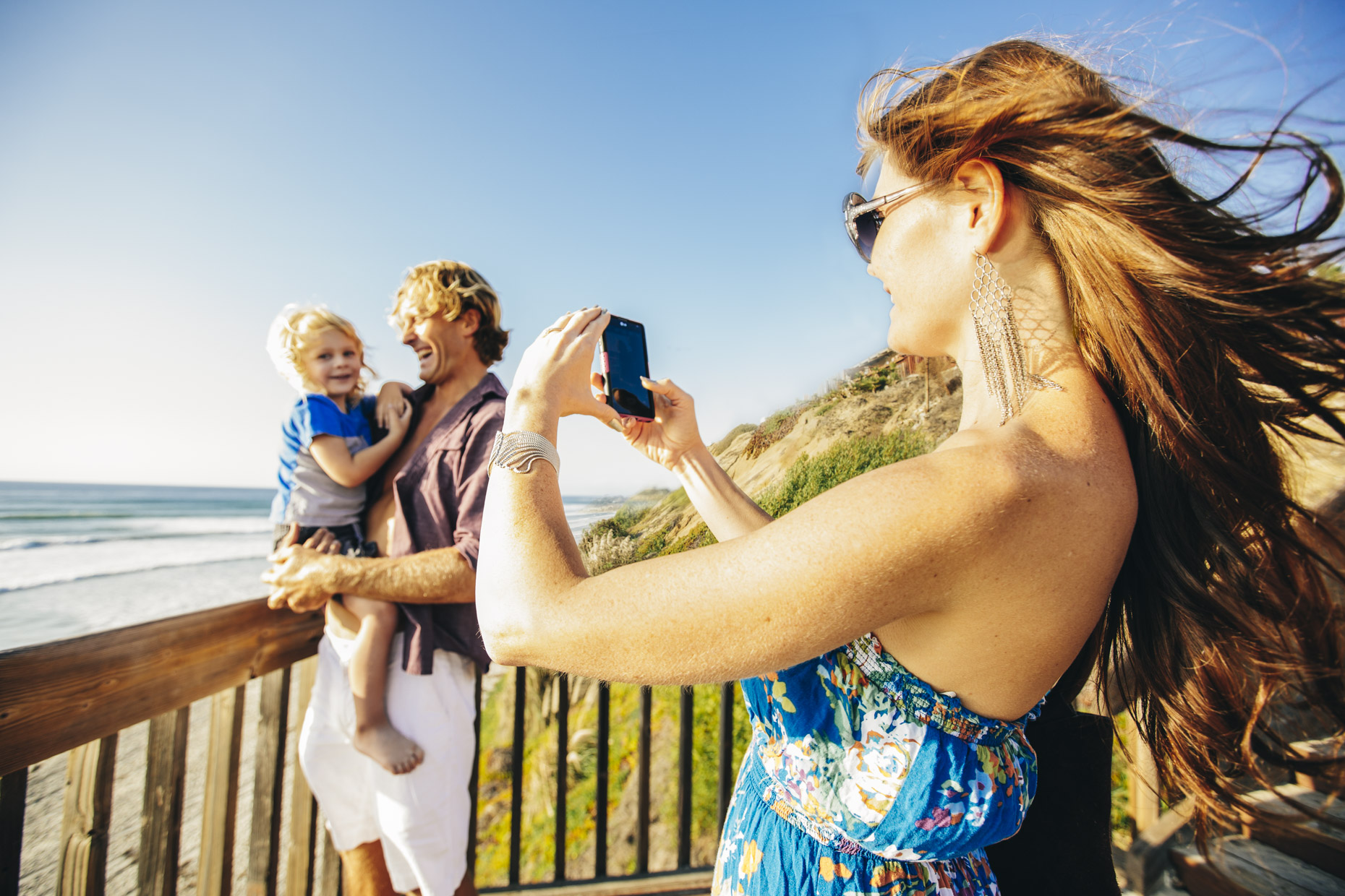 Woman taking photo of man and child on deck at the beach