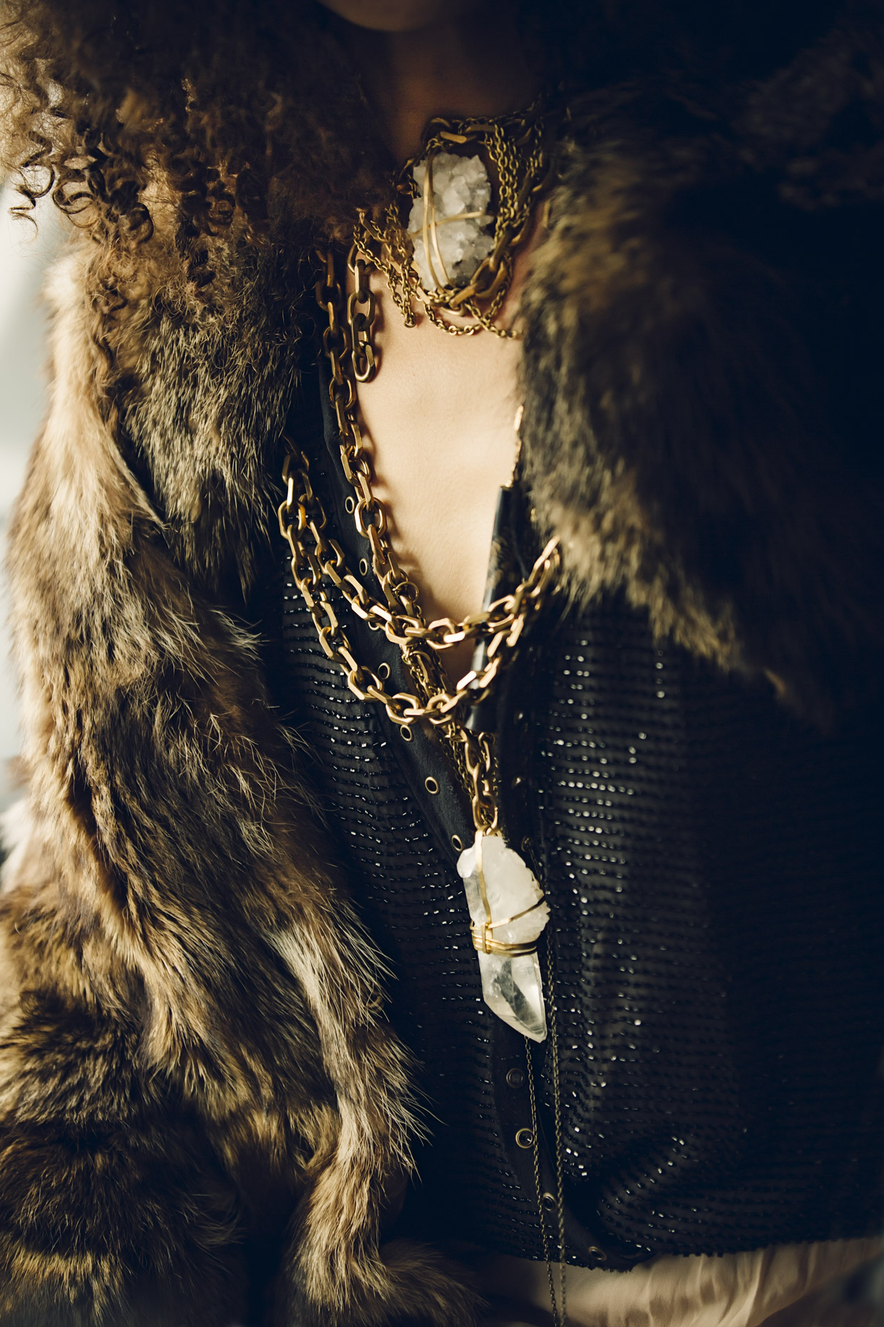 Woman in black v-neck shirt, fur coat with brass and white crystal Belthazzar Jewels necklaces