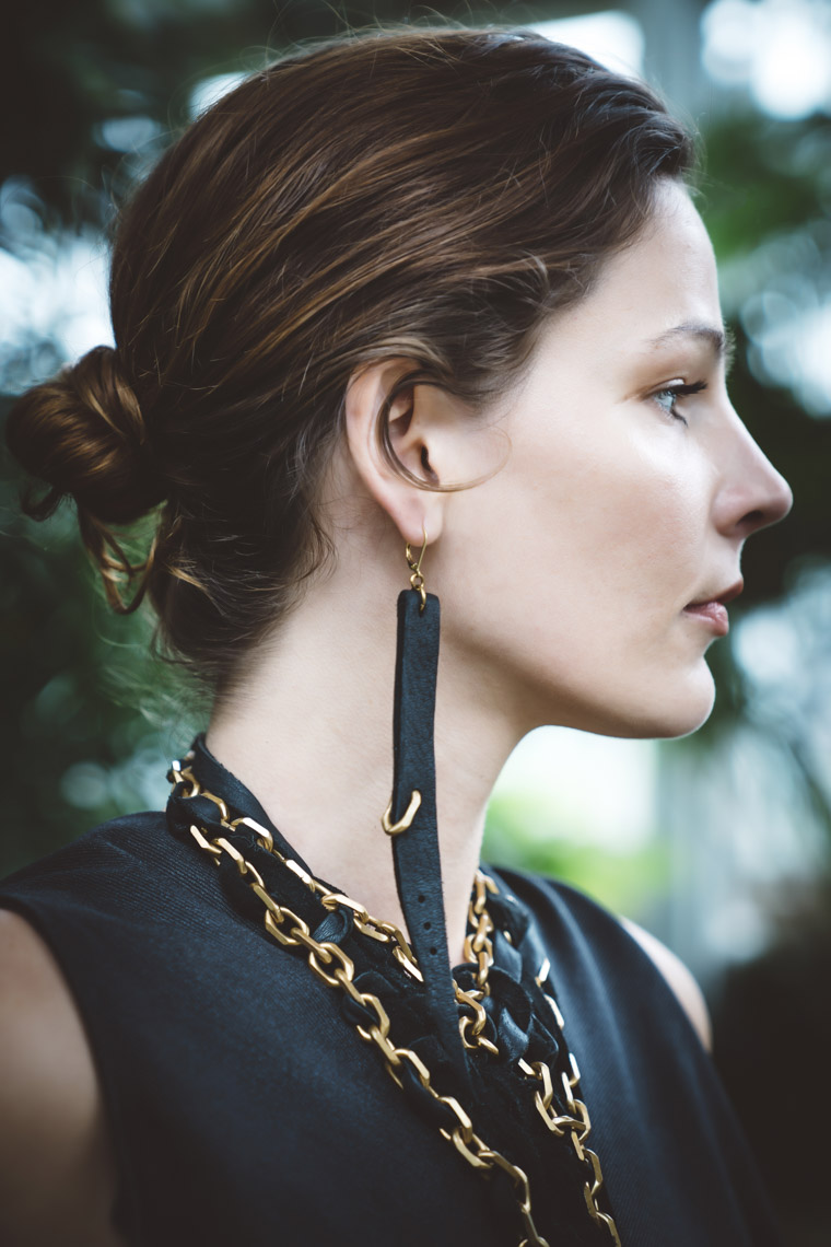 Woman wearing necklace earrings of brass and black leather