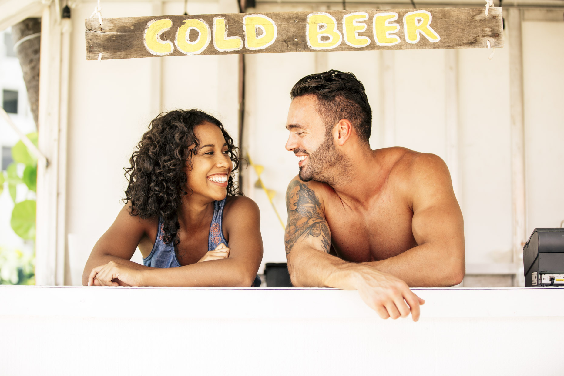 Man and woman laughing and talking under cold beer sign