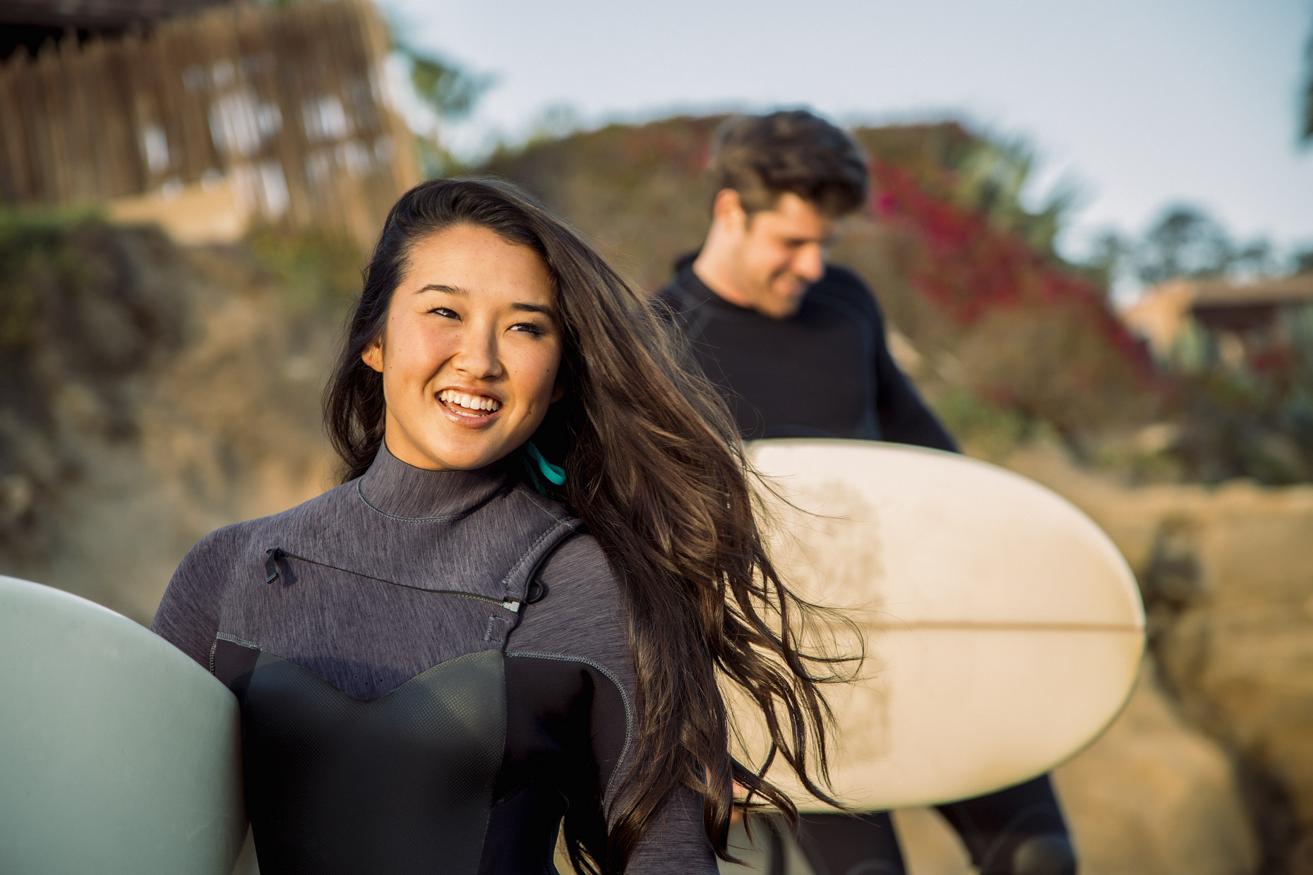 Happy woman and man in wetsuits carrying surfboards