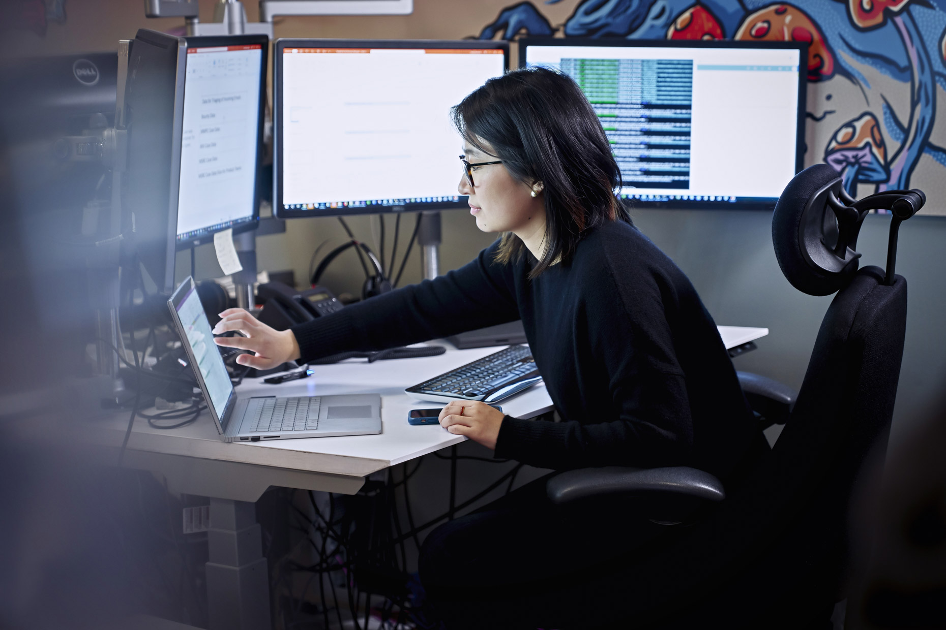 Woman working on touch screen laptop in front of bank of monitors